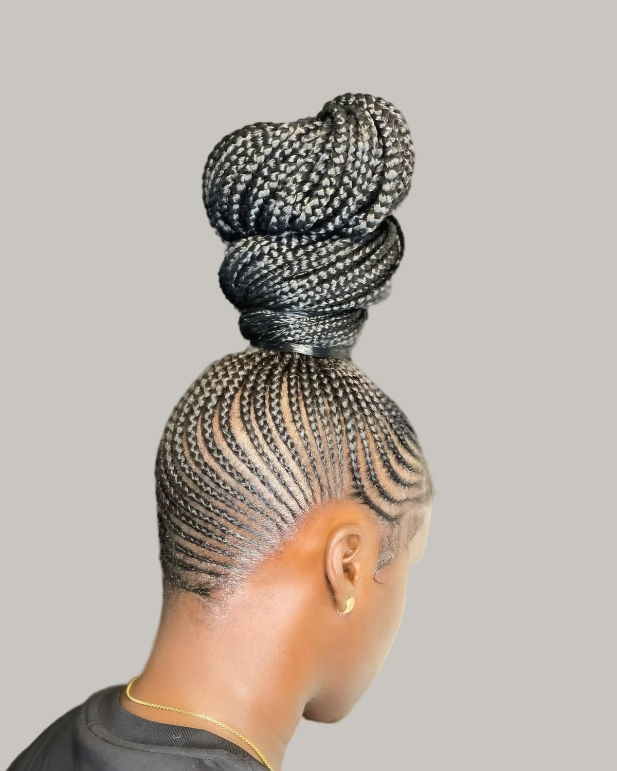 Woman in profile with braids wound into a high bun above cornrows