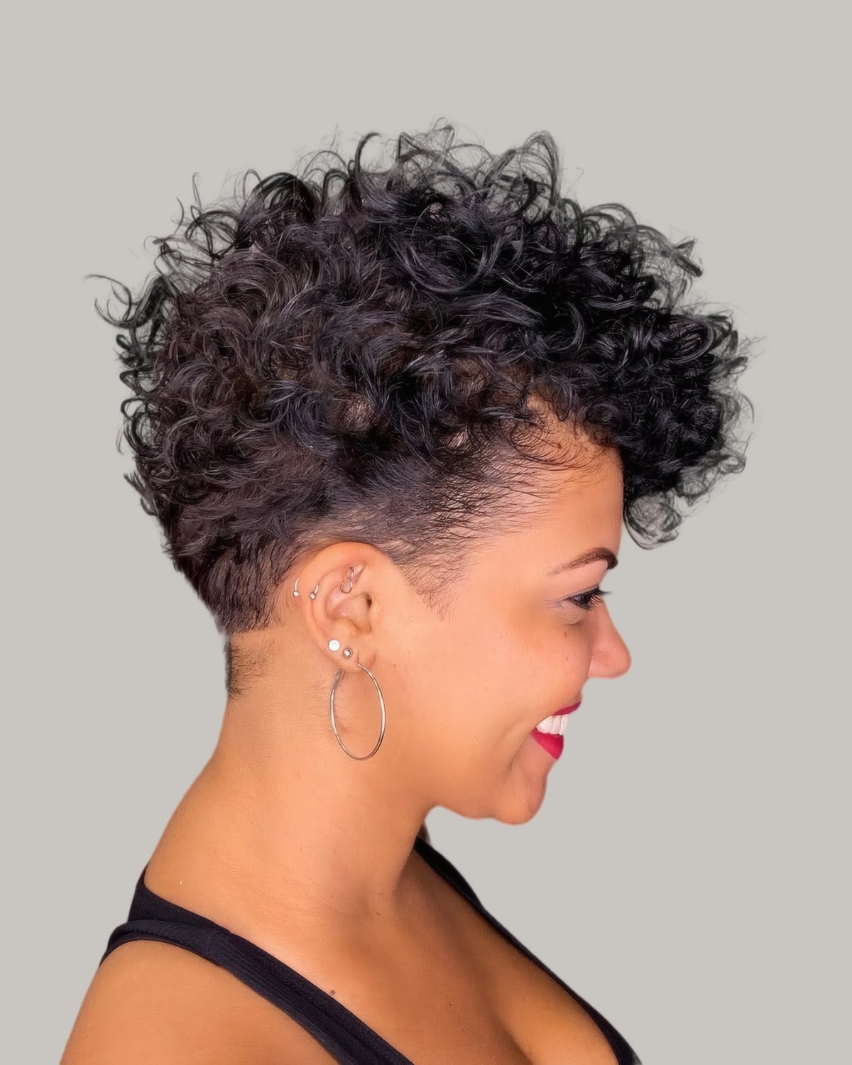 Smiling woman in profile with a short curly pixie, tapered at the sides