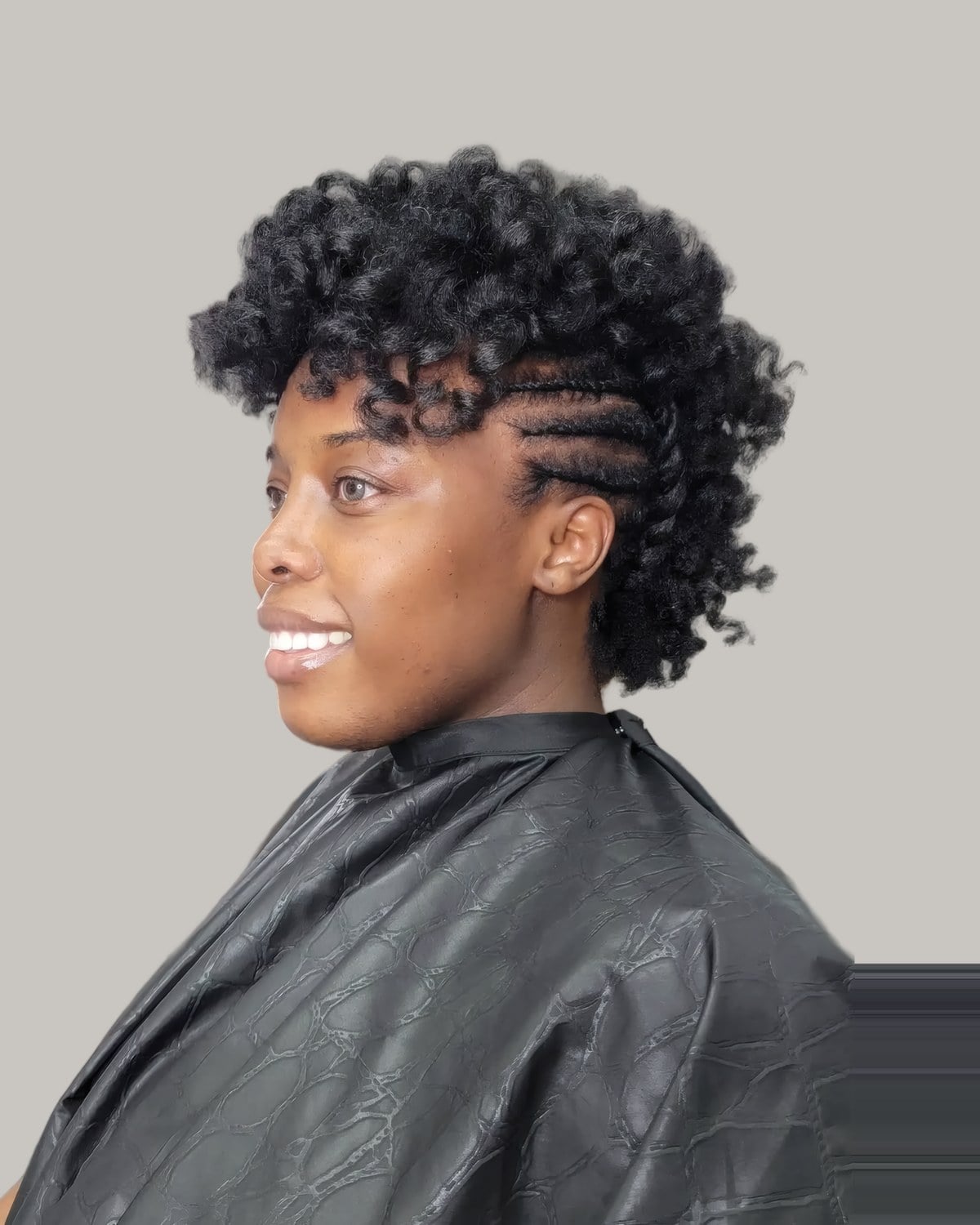 Smiling woman in a salon cape with a curly frohawk and braided sides