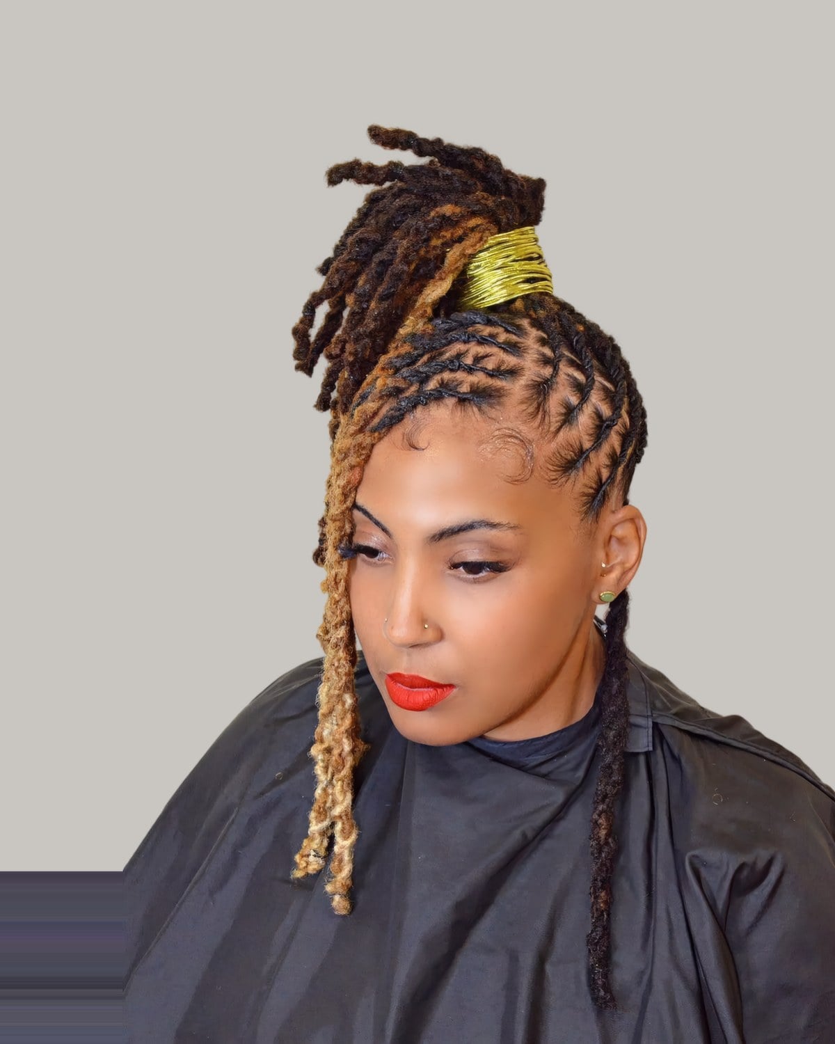 Woman in a salon cape with locs gathered into a top knot with a gold cuff