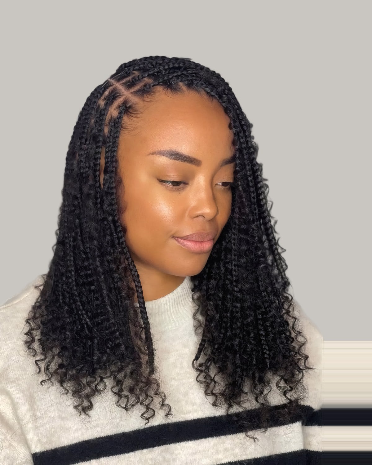Woman in a cream sweater with long knotless braids and curly ends