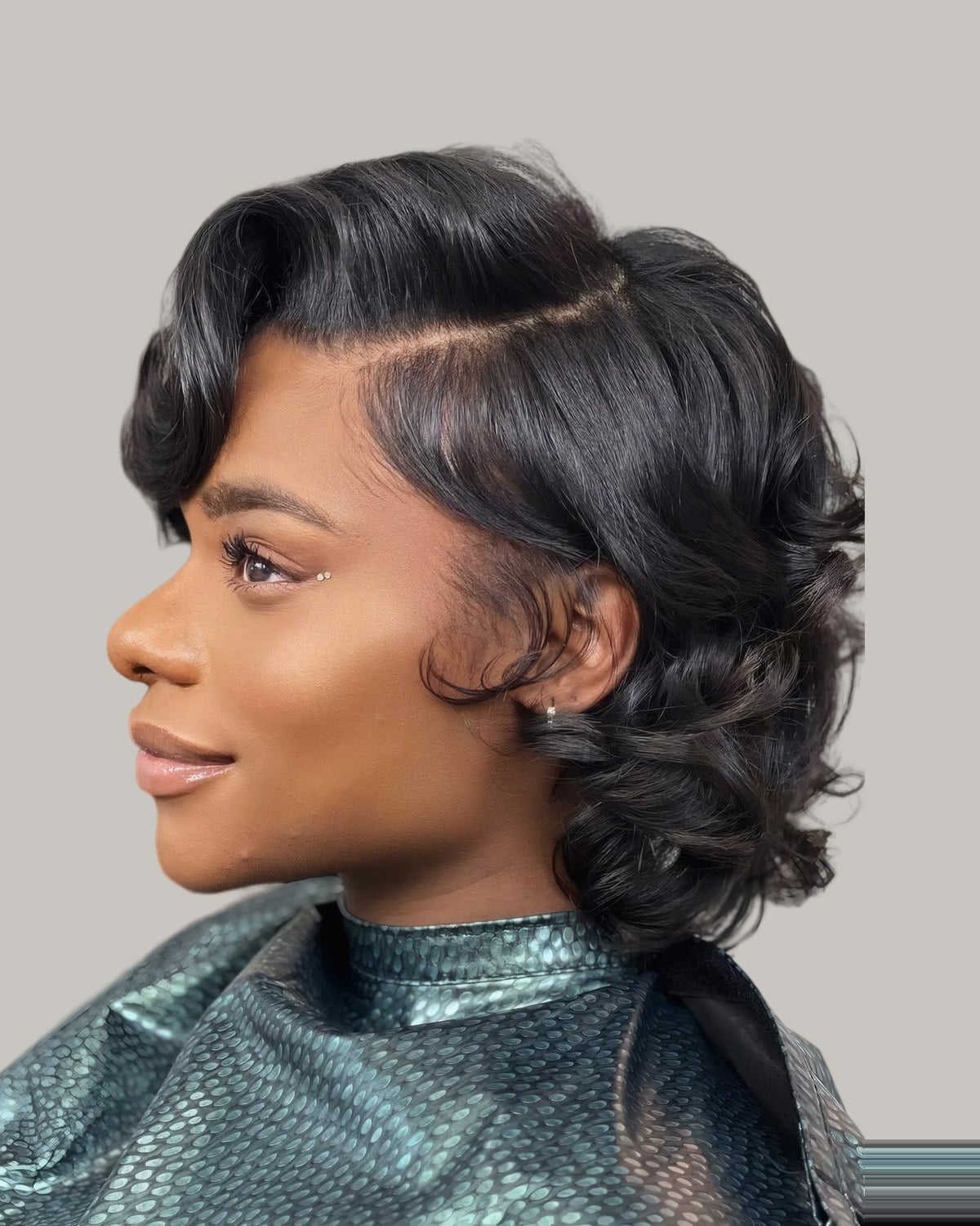 Woman in a salon cape with a side-parted curly bob