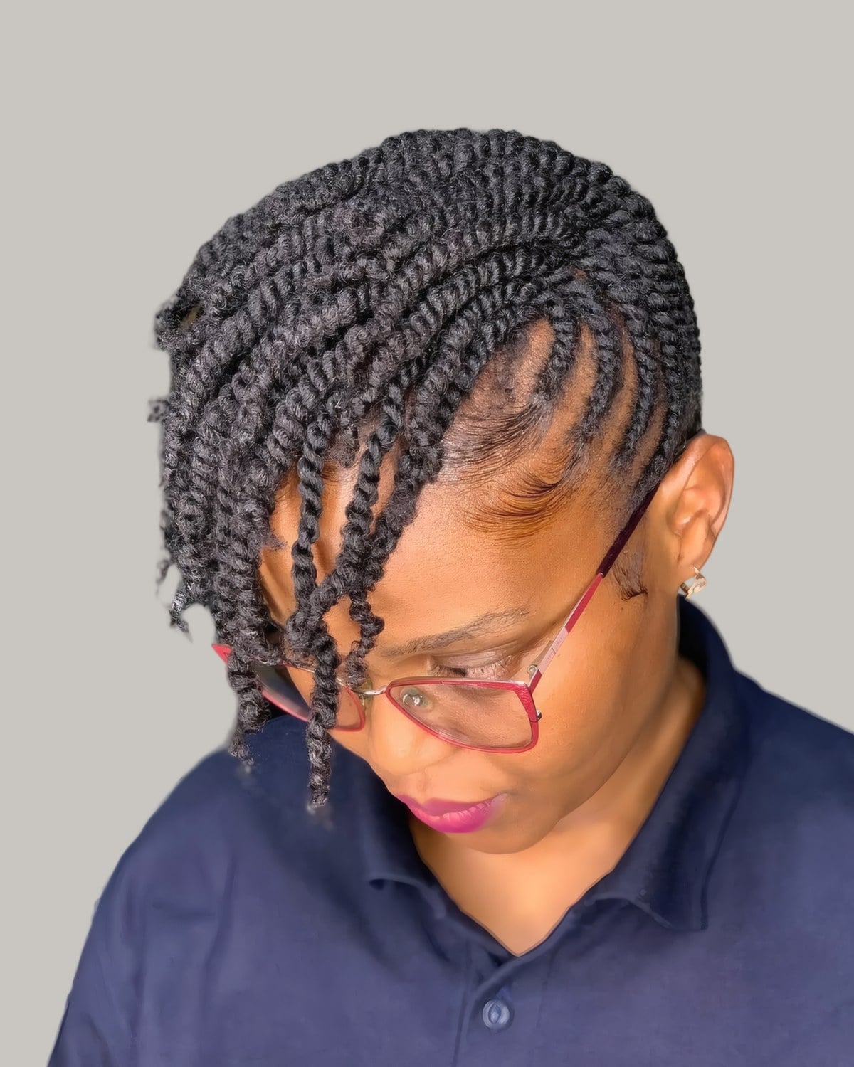 Woman in glasses with short two-strand twists, looking down