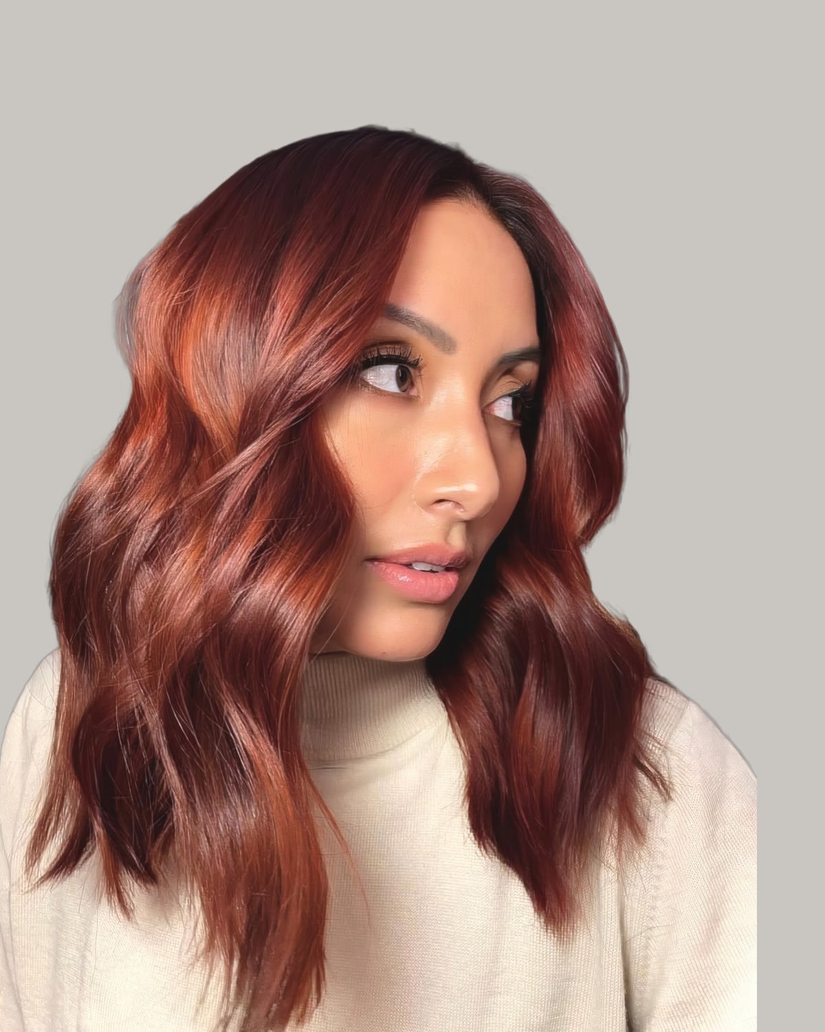 Woman in a cream sweater looking over her shoulder with auburn waves