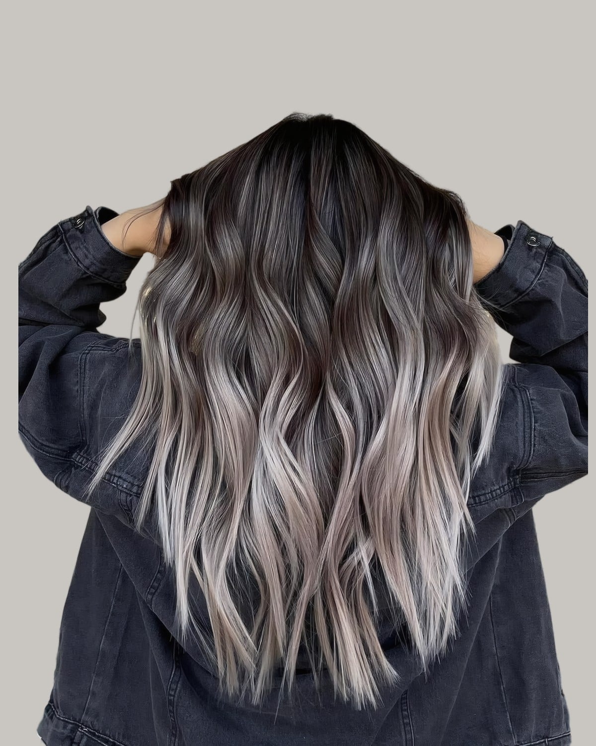 Woman in a denim jacket seen from behind, hands on her head, with icy blonde balayage