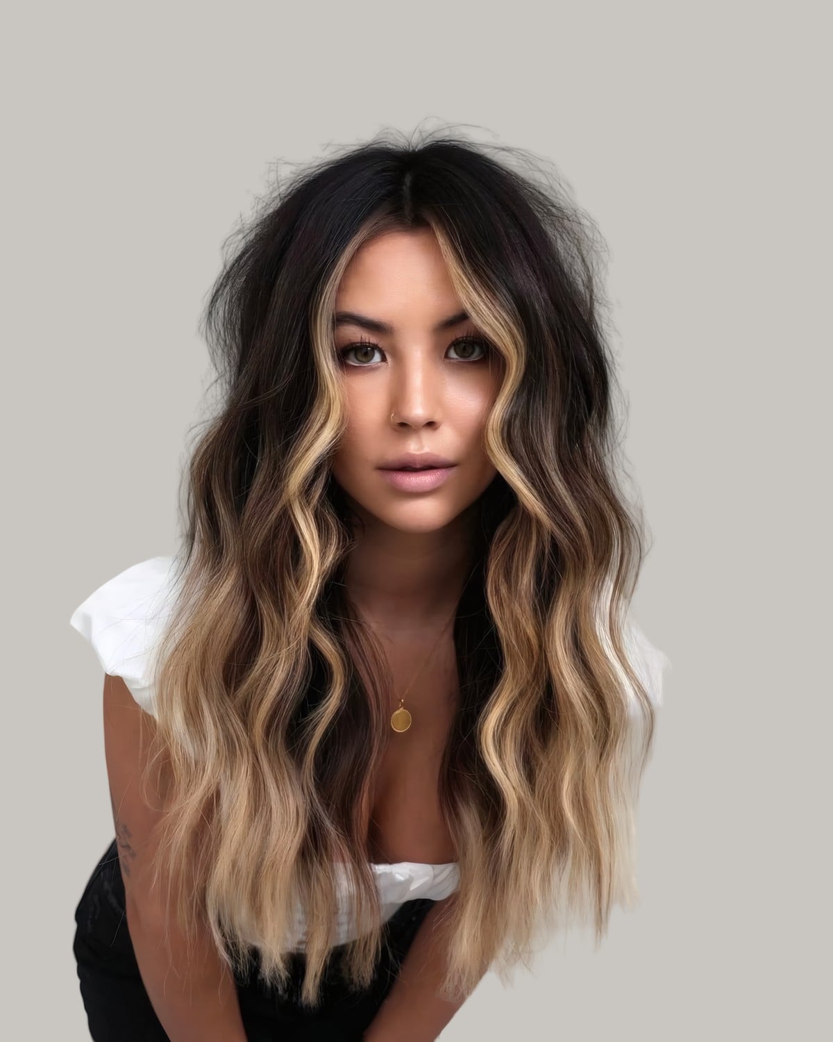 Woman leaning forward with a dark root and caramel blonde waves framing her face
