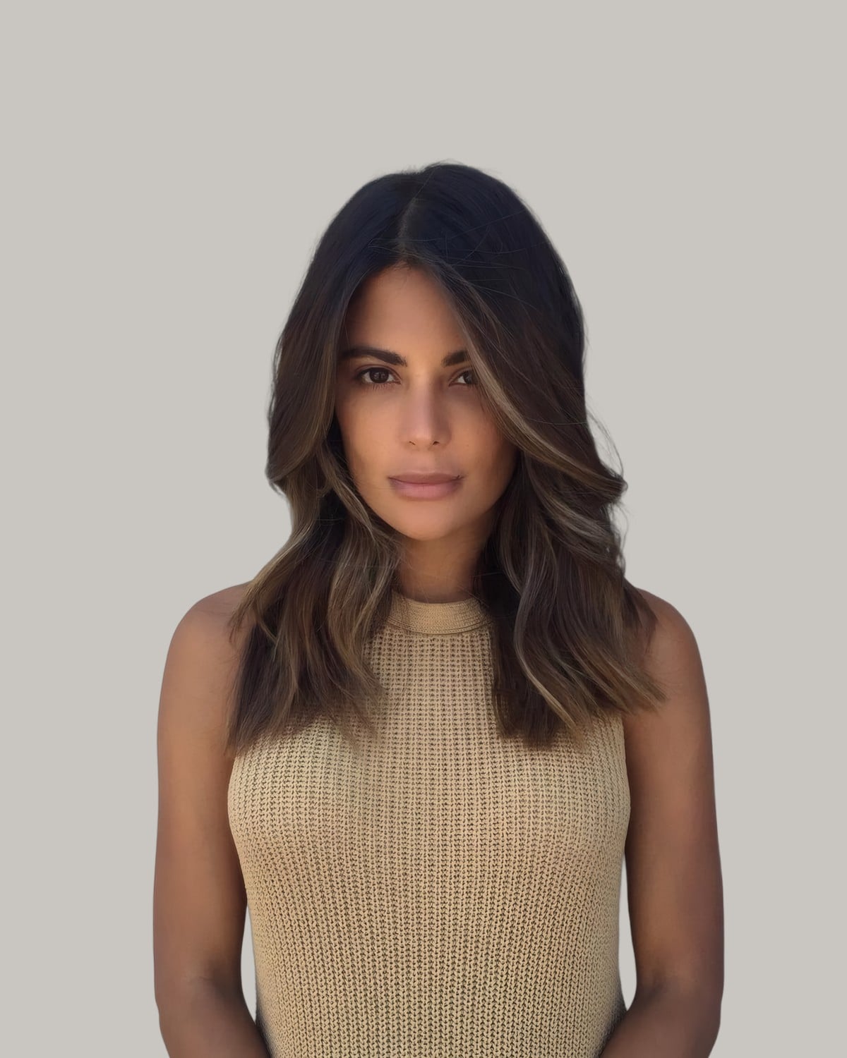 Woman in a beige top with a center part and dark brown hair with soft face-framing pieces