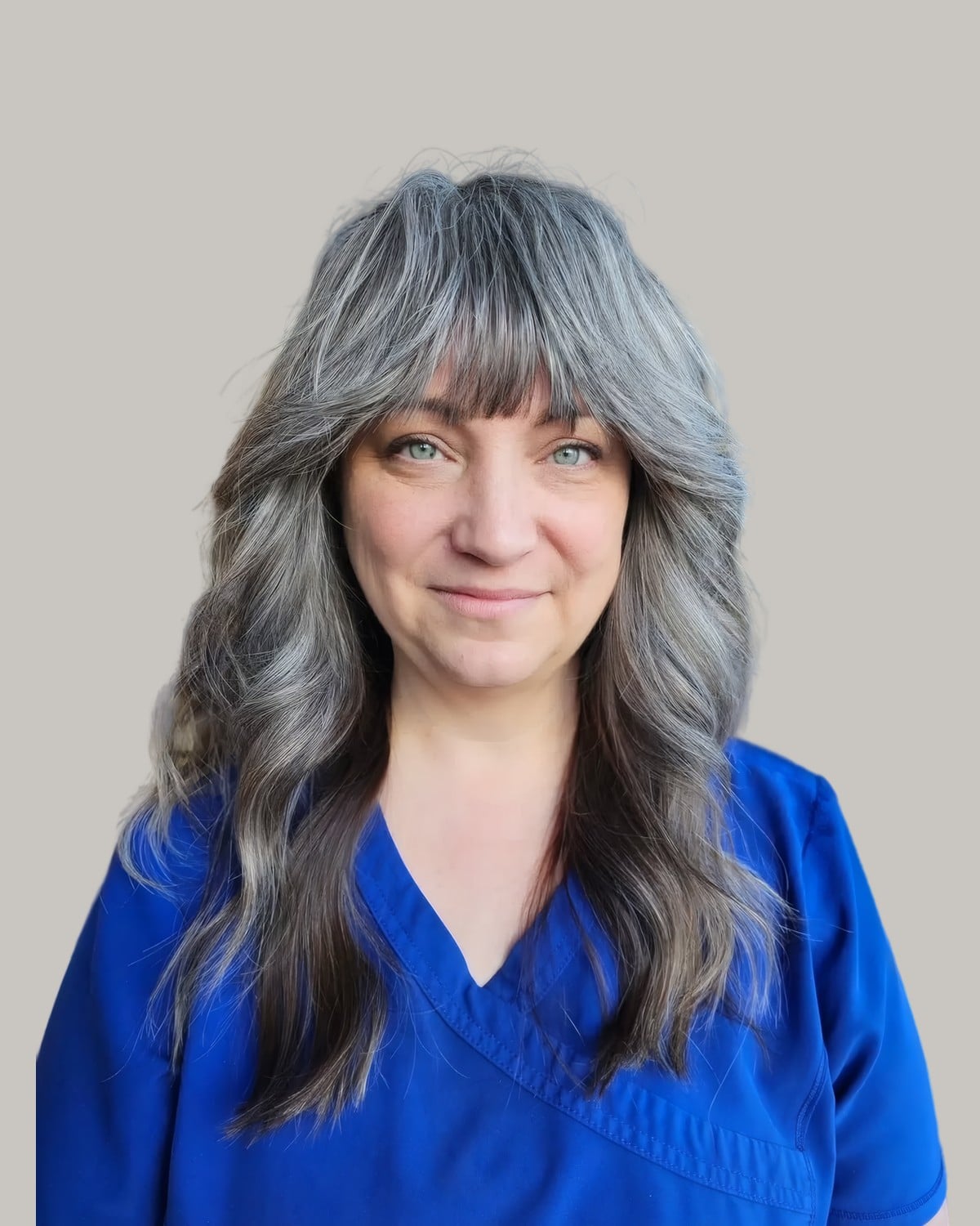 Smiling woman in blue scrubs with curtain bangs and gray waves