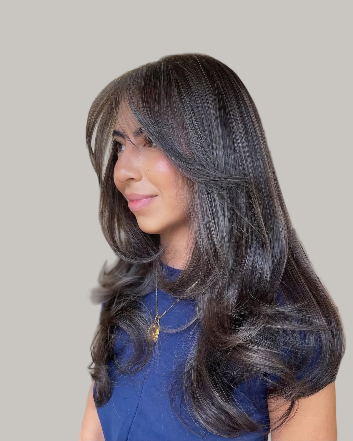 Woman in a blue top with long dark layers and silver face-framing strands