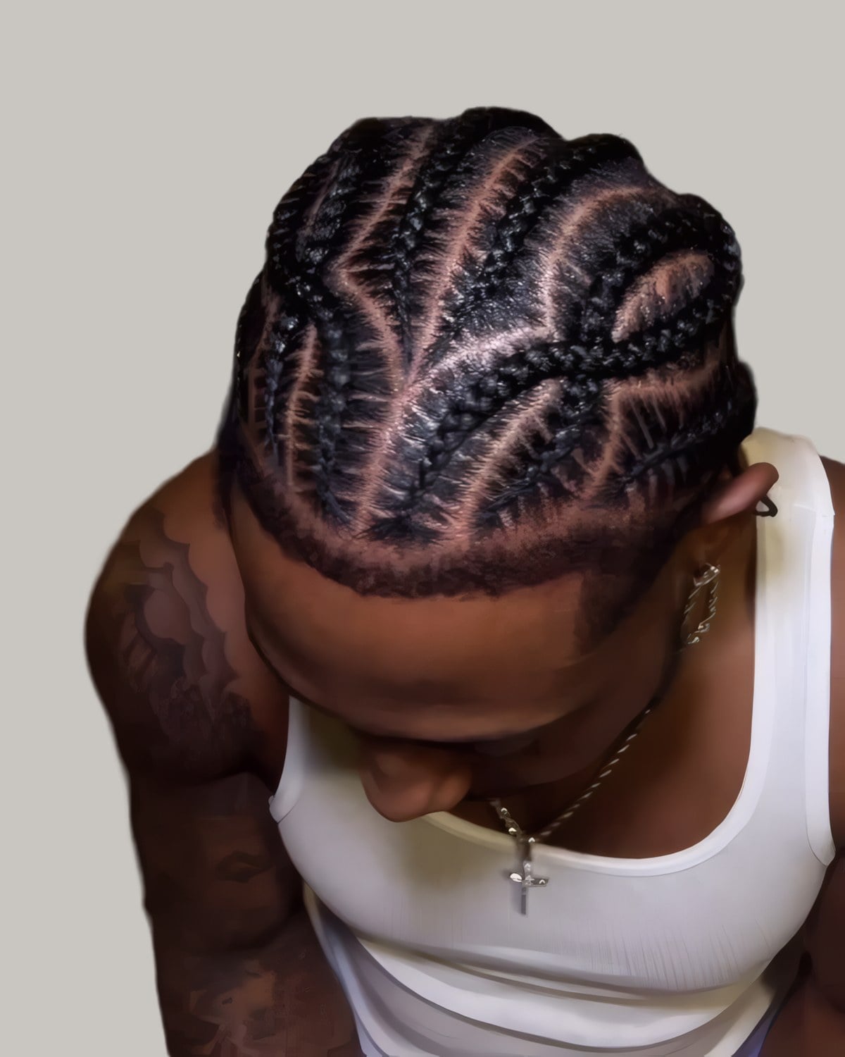 Man in a white tank top with curved cornrow designs, looking down