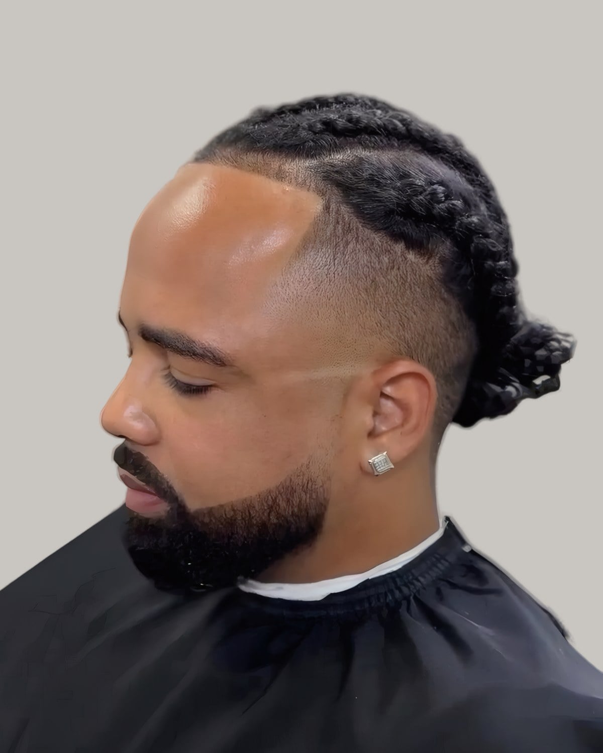 Bearded man with cornrows gathered into a bun, seen in profile