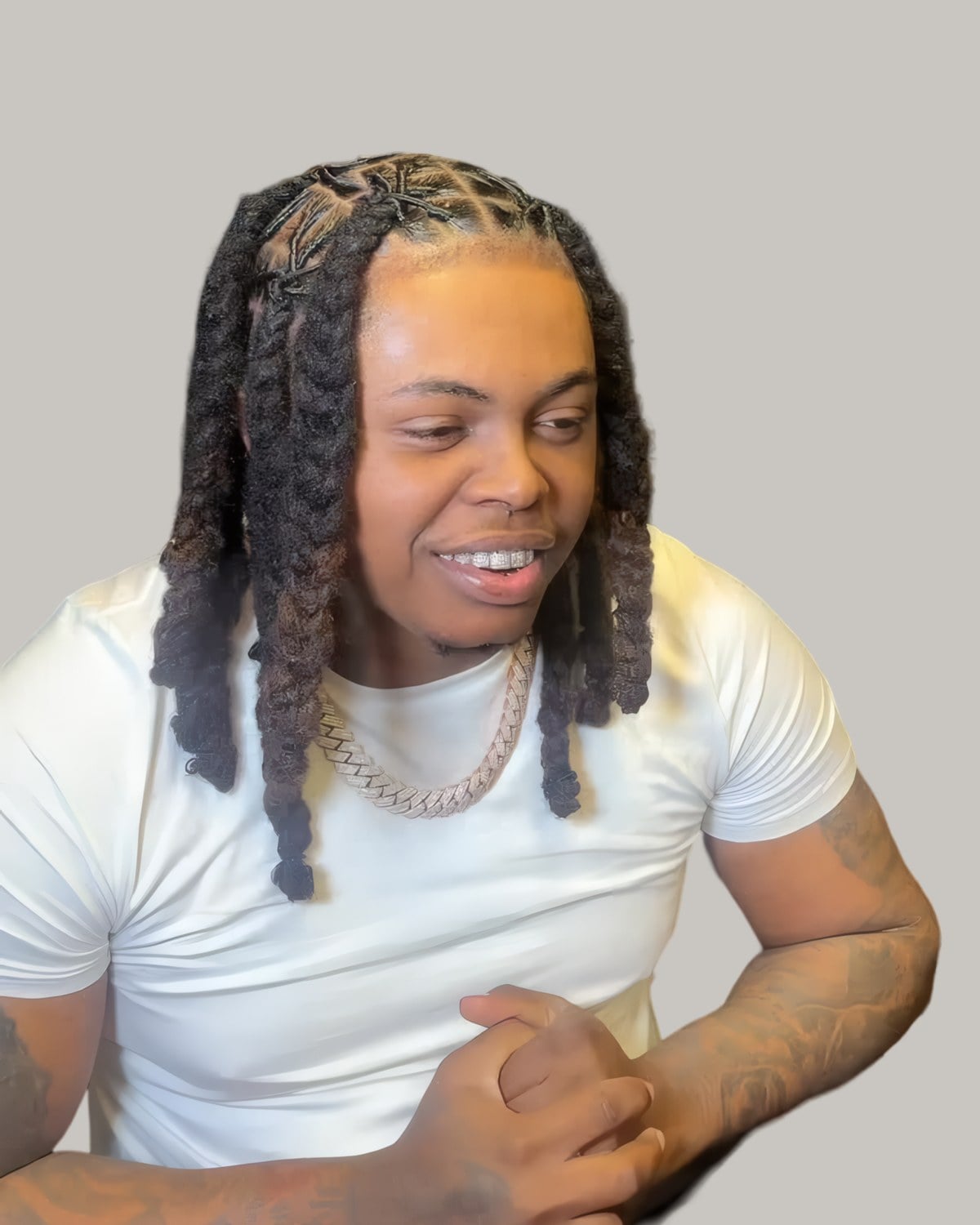 Smiling man with plaited locs hanging over his shoulders, seated