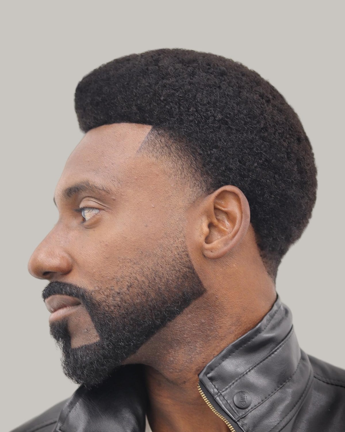 Bearded man with a rounded afro and a sharp line-up, in a black leather jacket, seen in profile