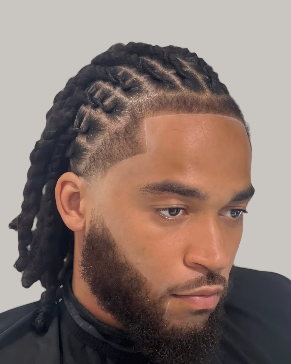 Bearded man with two-strand twists pulled back, seen at an angle