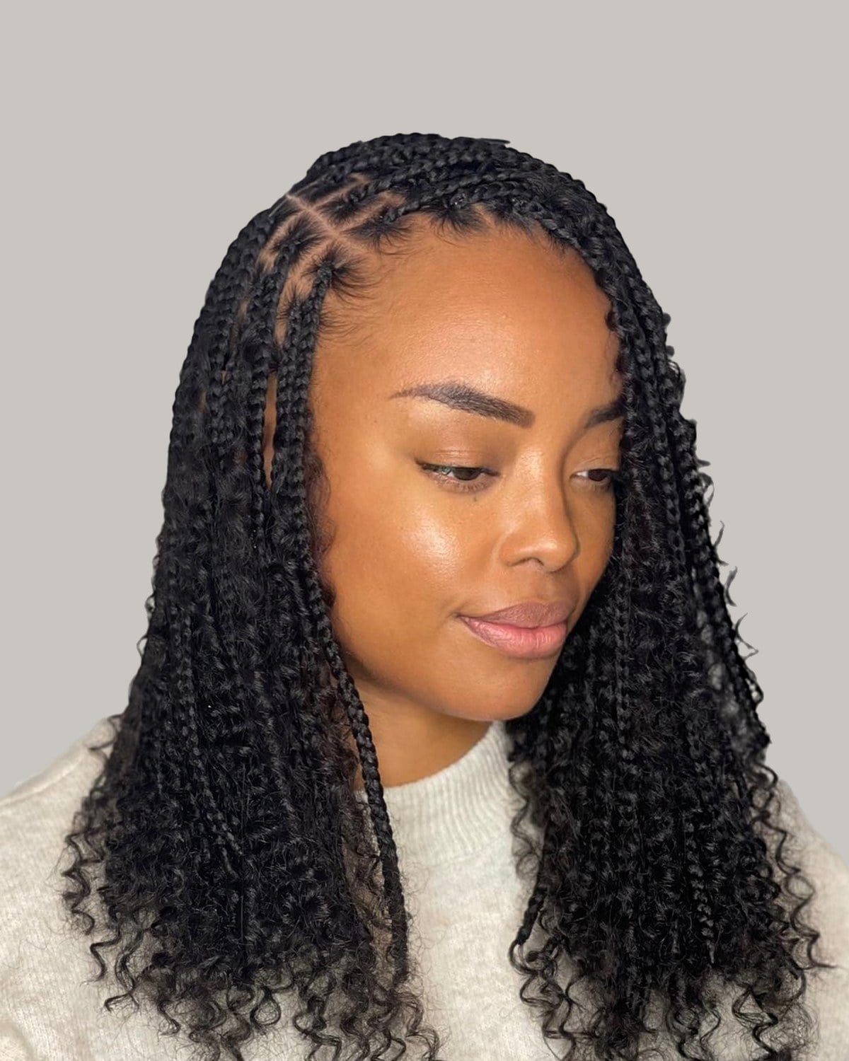Woman in a cream sweater with black boho knotless braids to mid-back