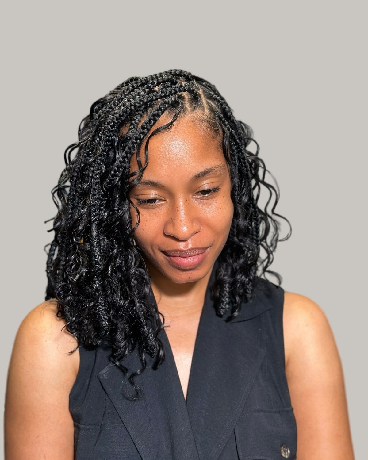 Woman looking down with black Bora Bora braids to the collarbone, in a black vest