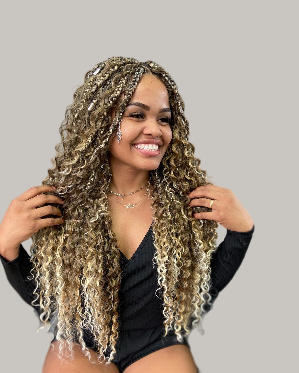 Smiling woman with long blonde and brown Bora Bora braids, her hands in her hair