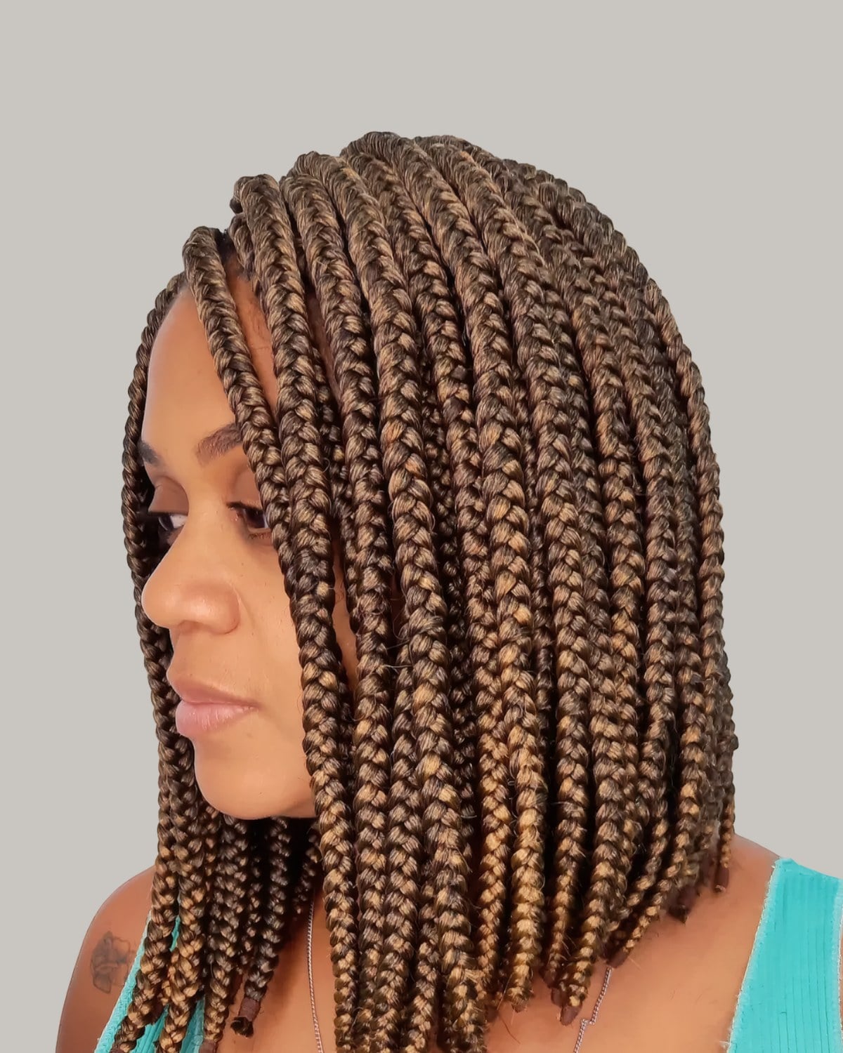 Woman in a green tank top in three-quarter view with a honey-brown box braid lob