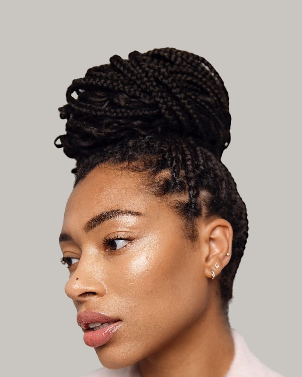 Woman in a white robe in three-quarter view with small braids in a high top knot