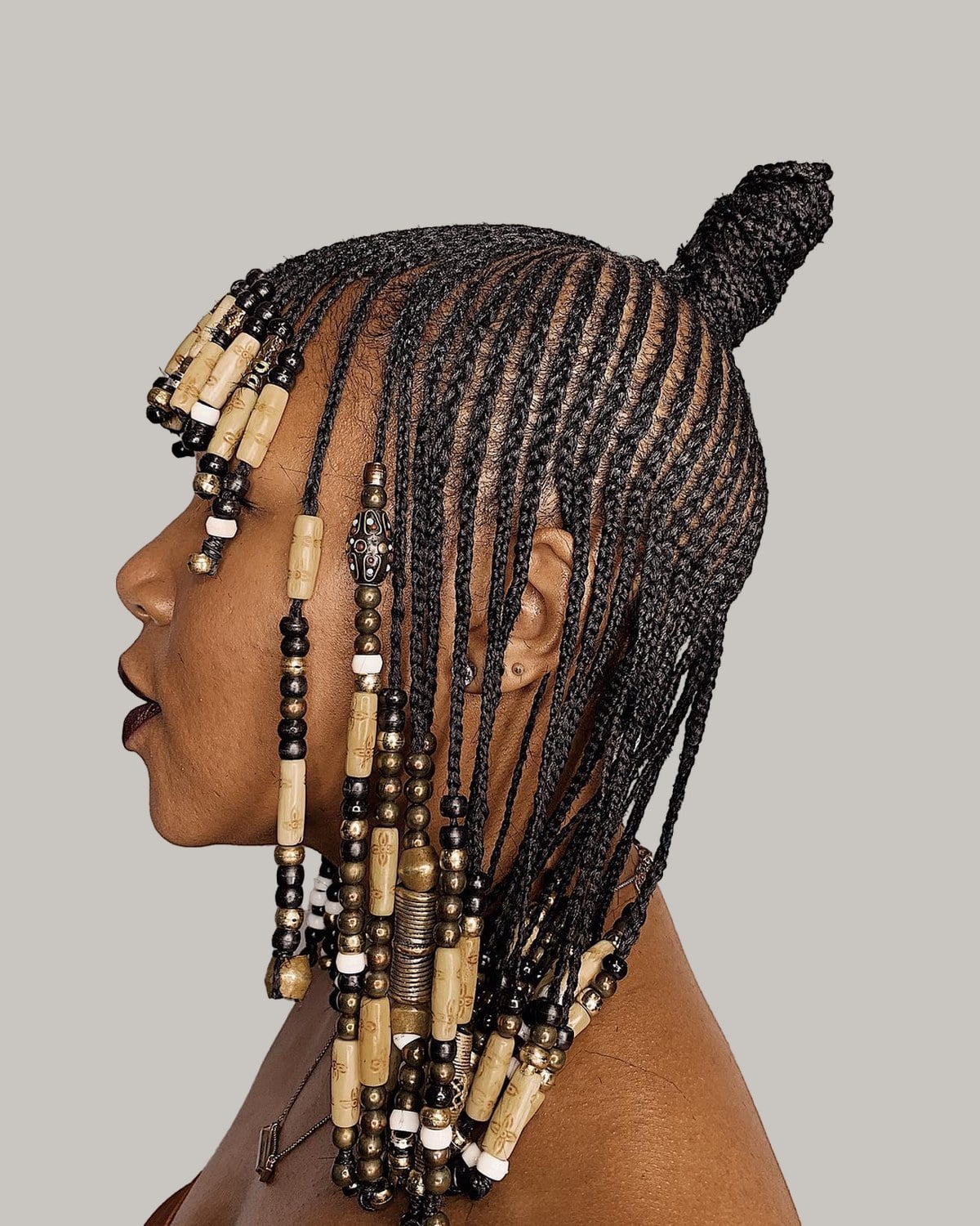 Woman in a brown off-shoulder top seen in profile, braids with wooden beads and a top knot