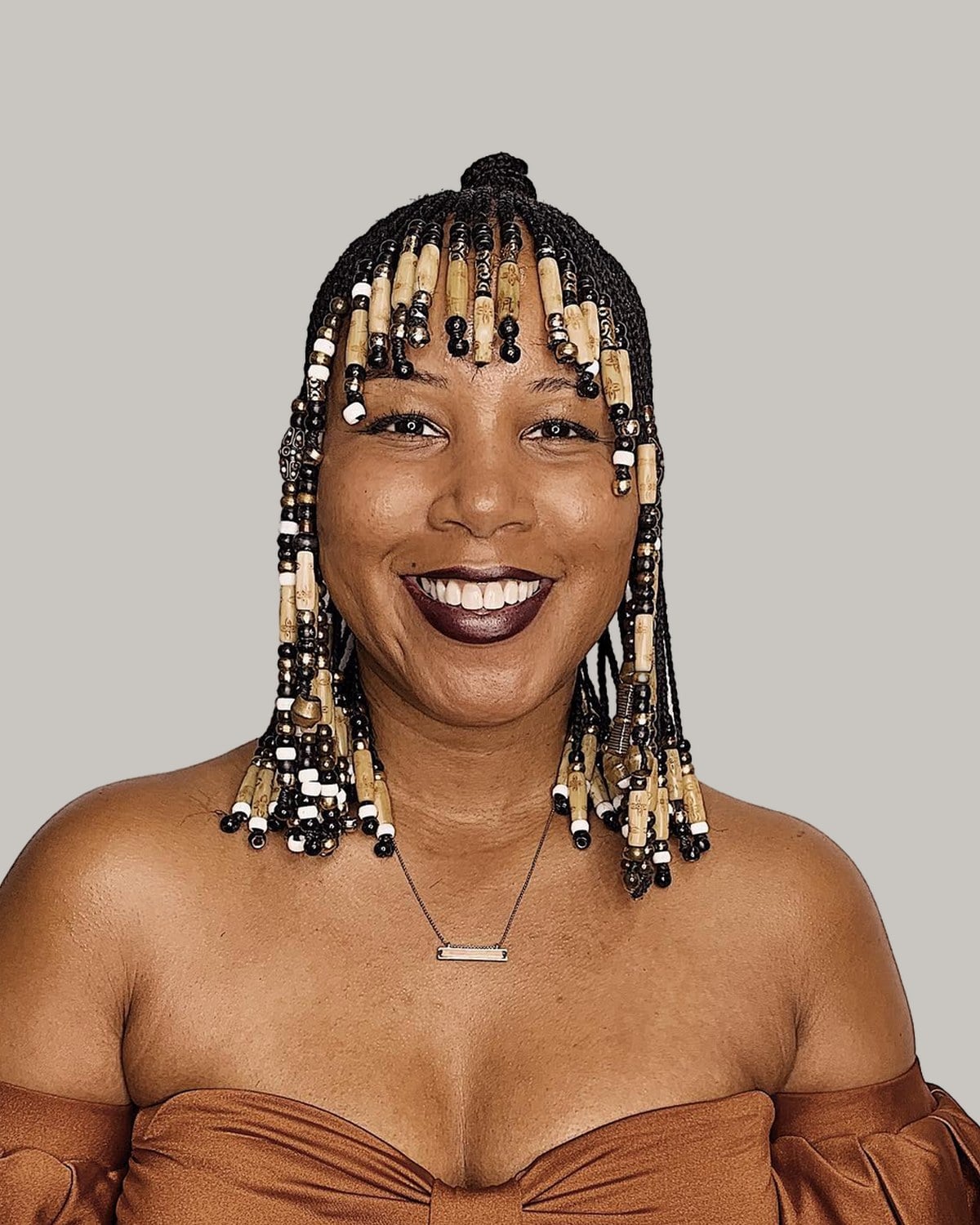 Woman in profile with a braided fringe stacked with wooden beads and a top knot