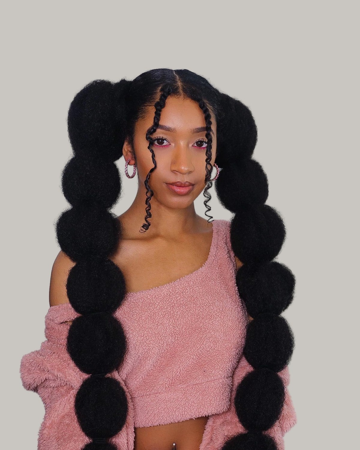 Woman with two long bubble pigtails on natural hair and curly face-framing strands, in a pink top
