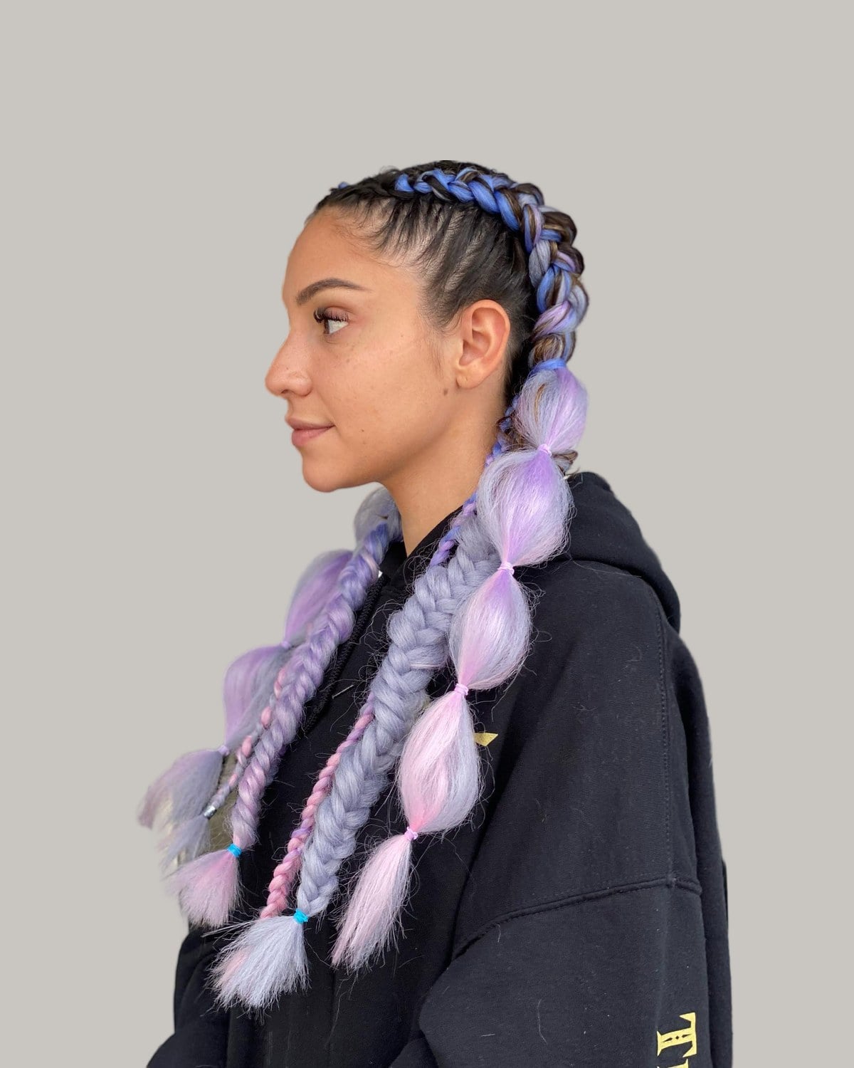 Woman in profile with cornrows and lilac bubble braids over a black hoodie