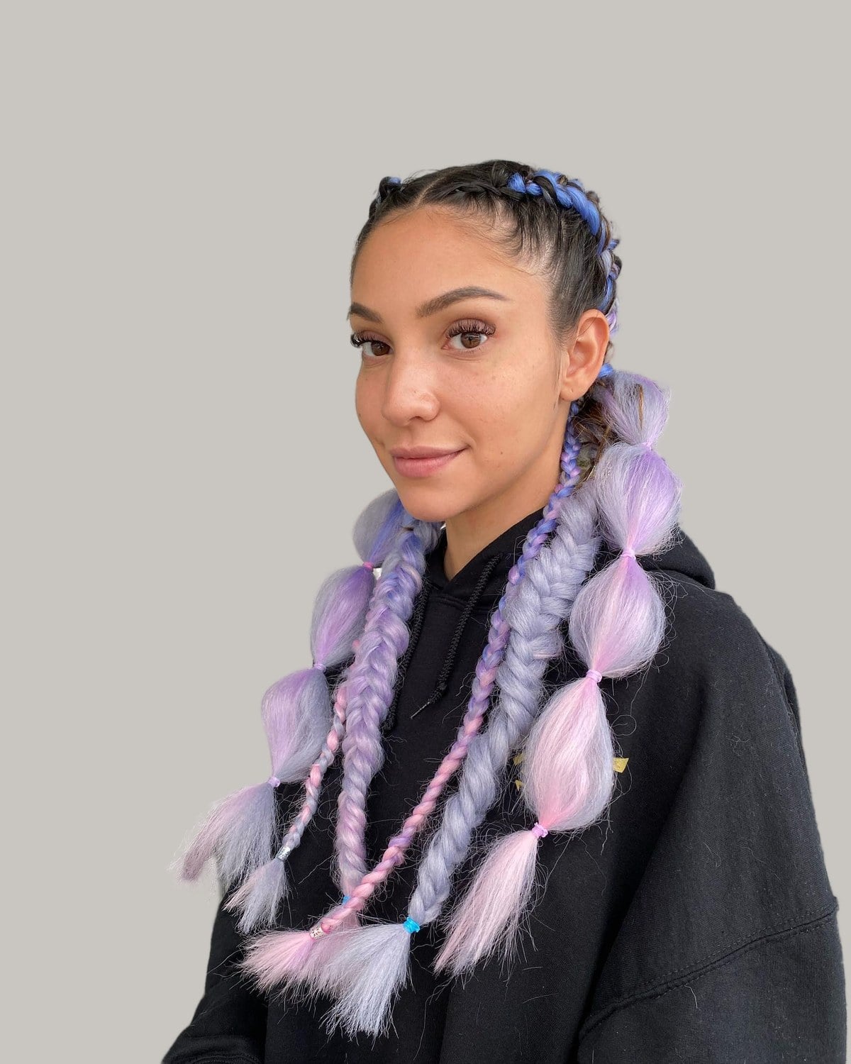 Woman with cornrows feeding into lilac and blue bubble braids, in a black hoodie