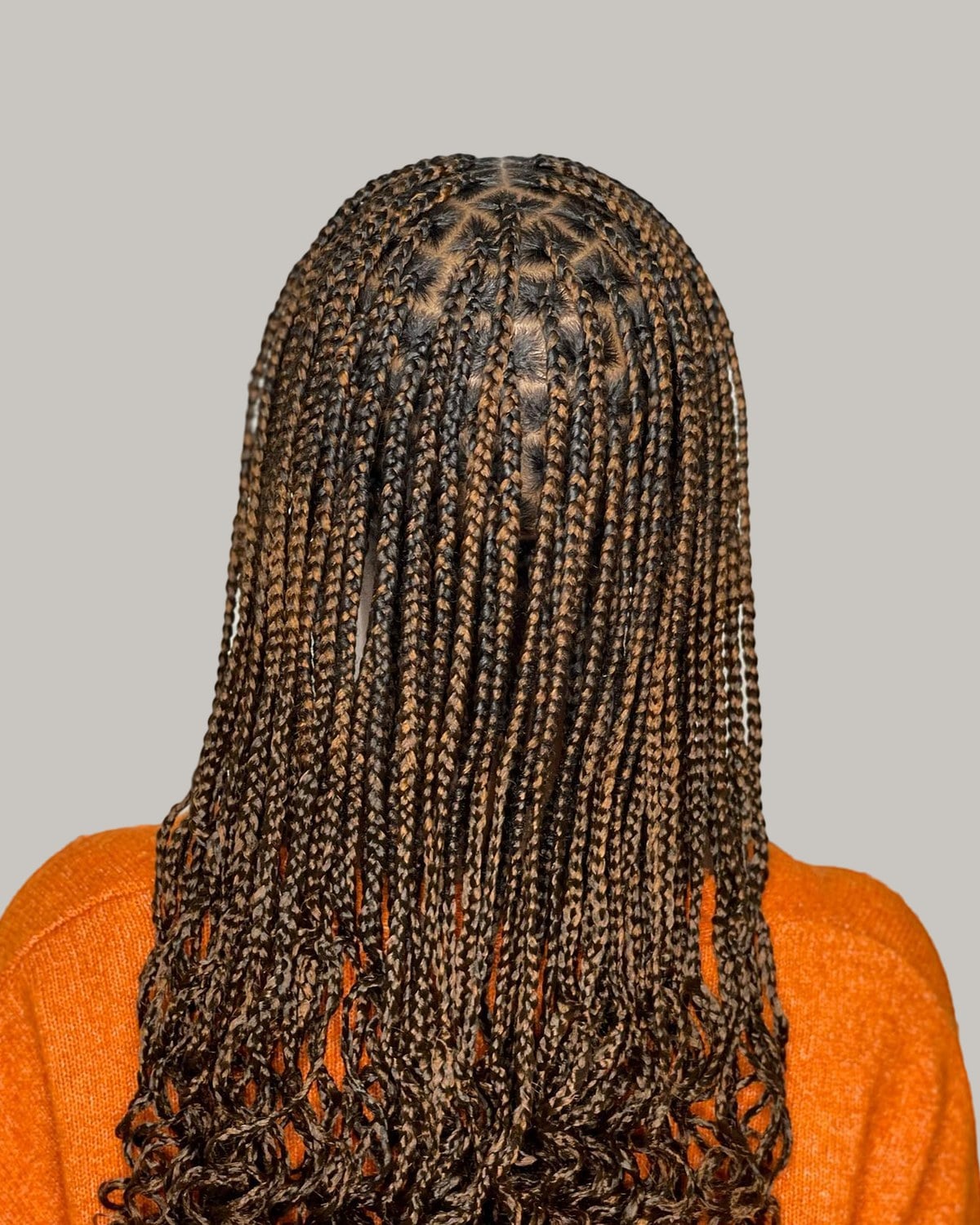 Back view of brown French curl braids over an orange cardigan