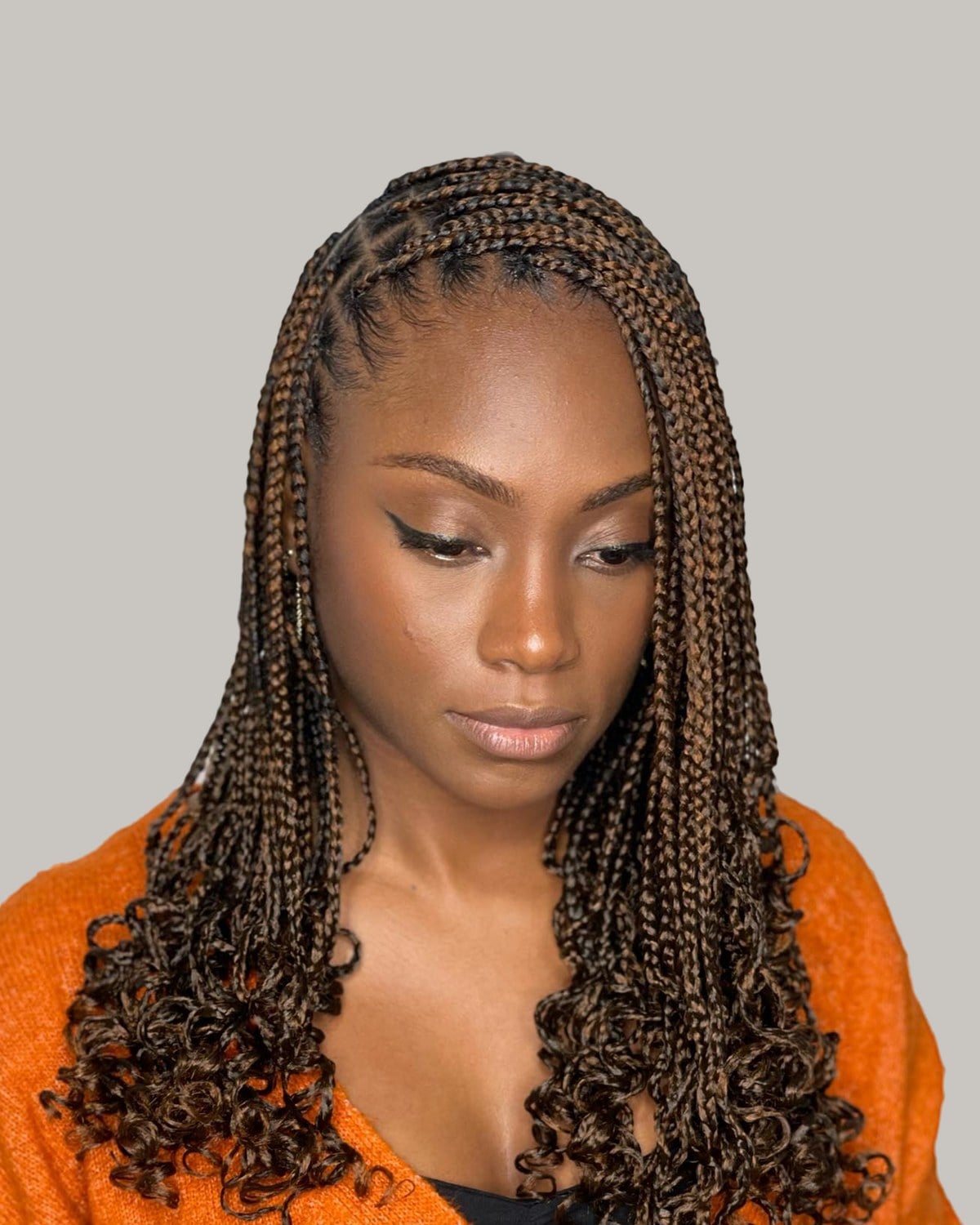 Woman in an orange cardigan with brown French curl braids to the chest
