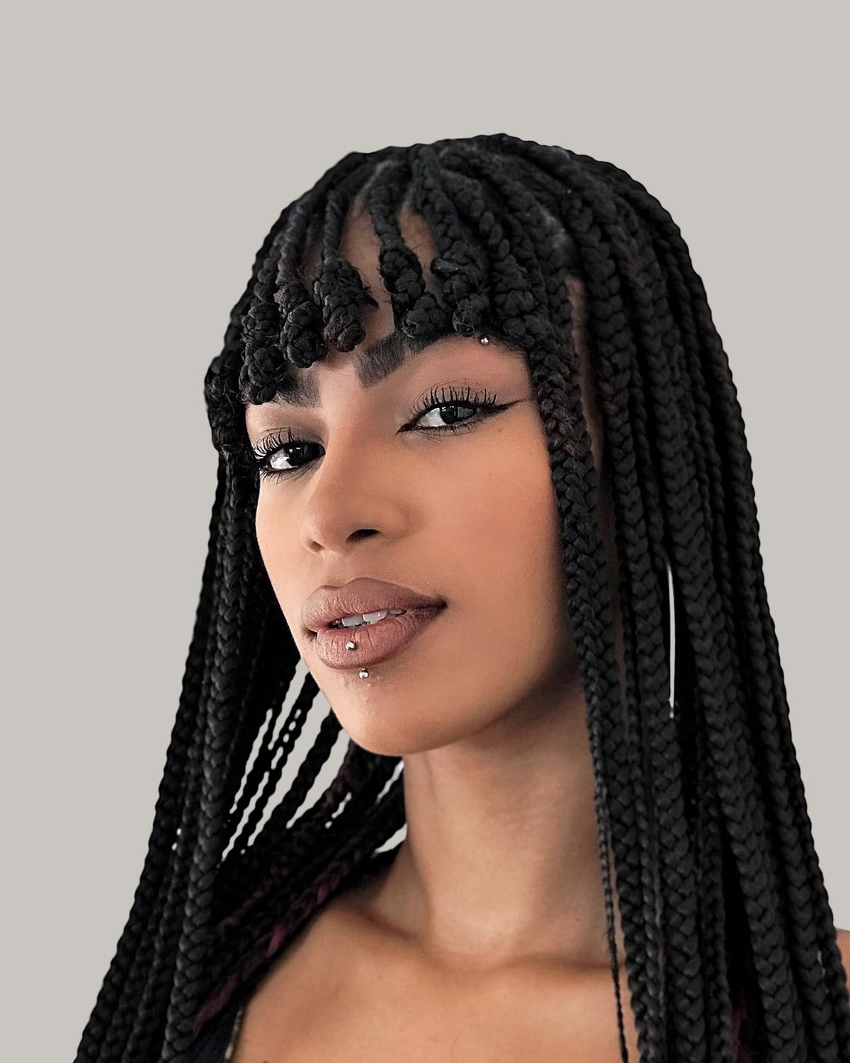Woman in a black top with long jumbo box braids and braided bangs