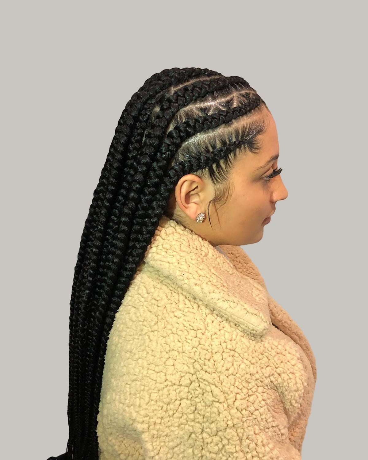 Woman in a cream sherpa jacket seen in profile with jumbo tribal braids past the waist