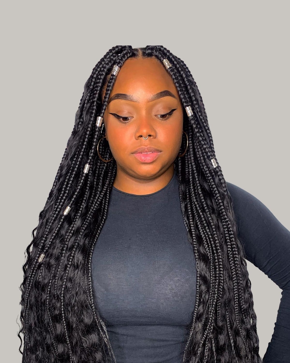 Woman in a black top looking down, waist-length black boho braids with silver cuffs