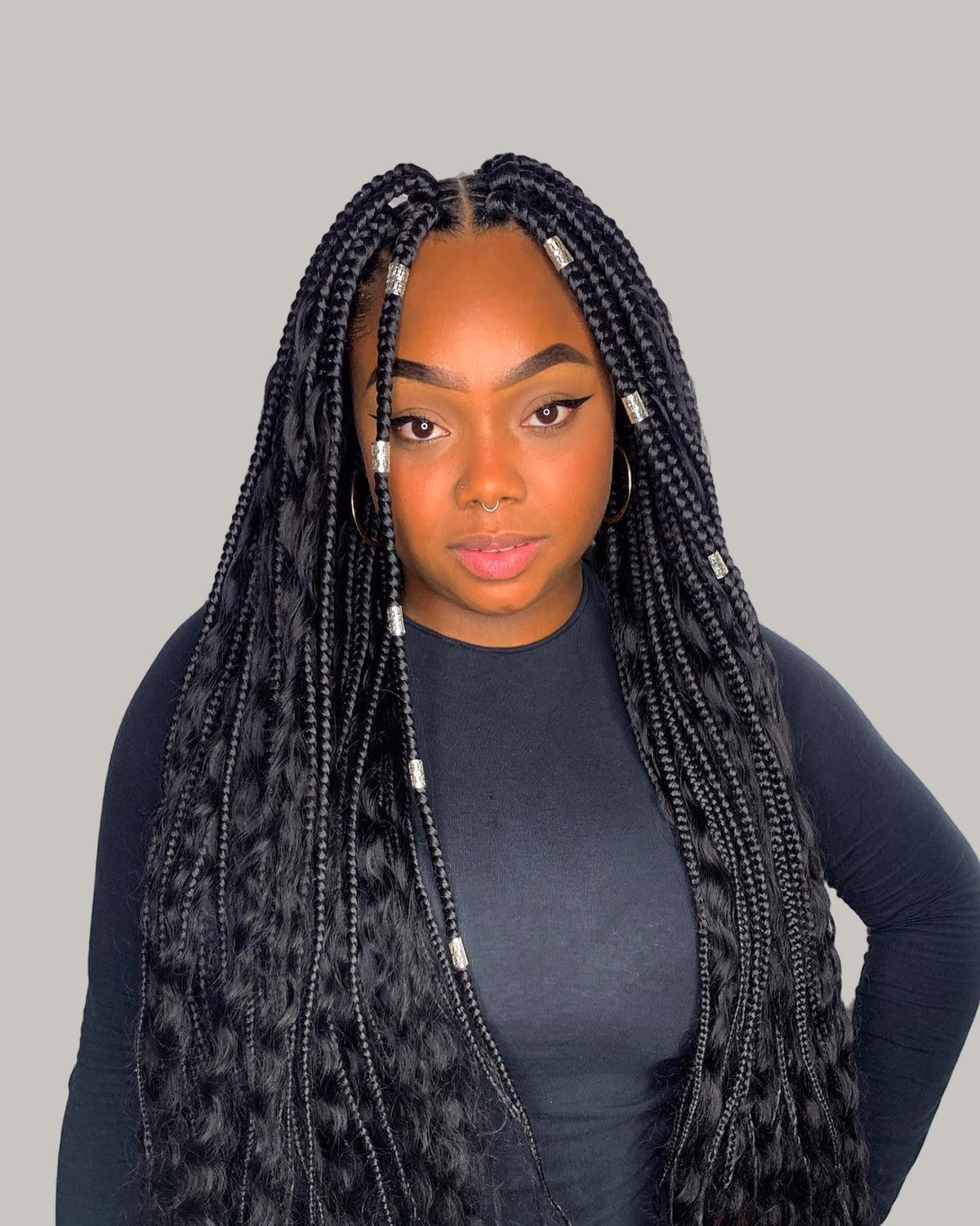 Woman in a black top with one hand on her hip and waist-length black boho braids with silver cuffs