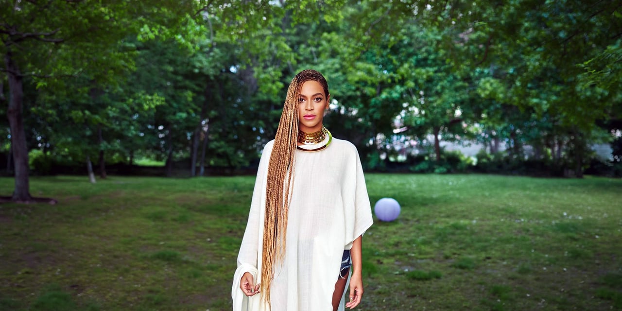 Woman with waist-length honey-blonde box braids, in a loose white dress, standing in a park
