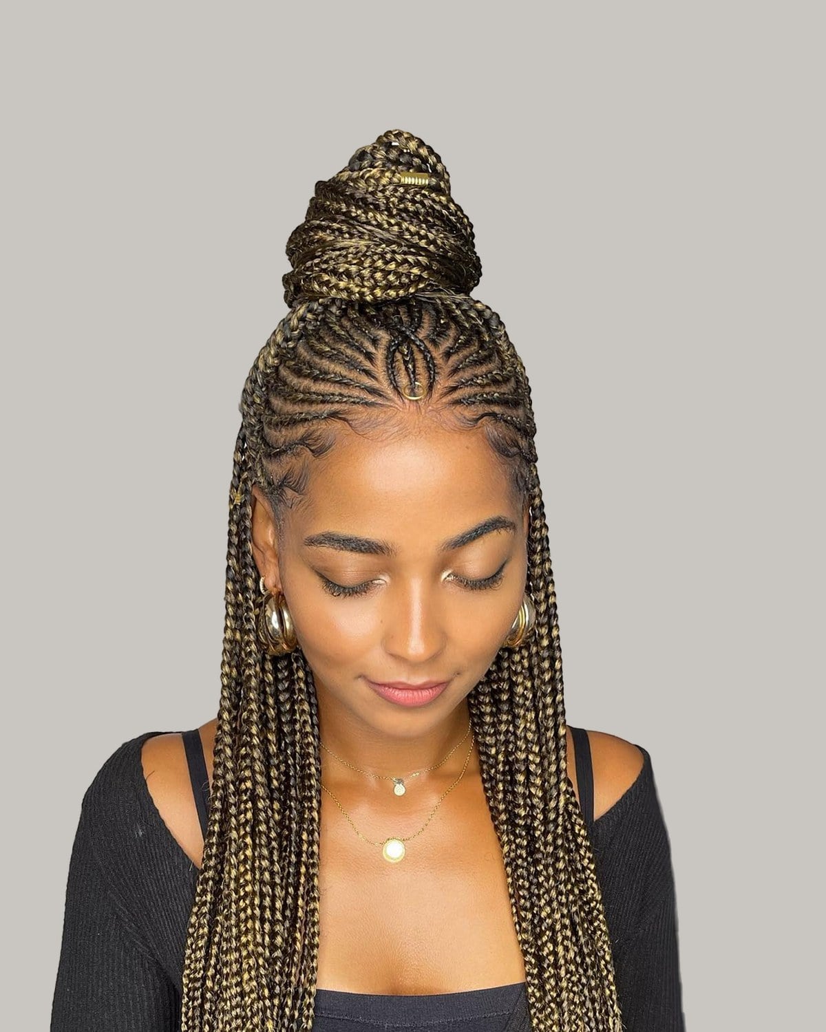 Woman in a black top with honey-blonde and black tribal braids, half up in a bun