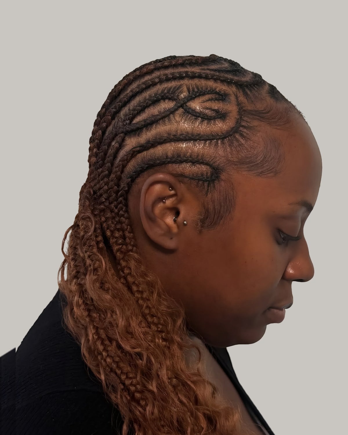 Woman looking down with swirled cornrows and copper braids with curly ends