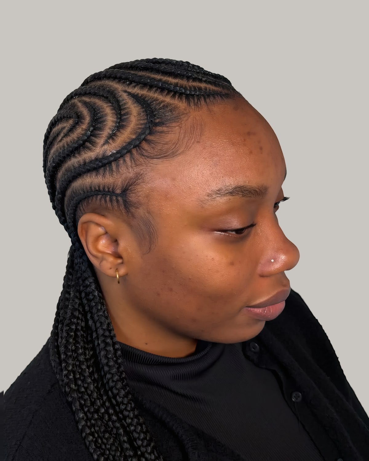 Woman in a black top in three-quarter view with black tribal braids and swirled cornrows