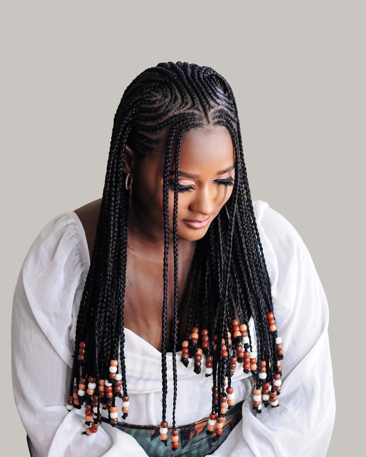 Woman in a white blouse looking down, black tribal braids with wooden beads