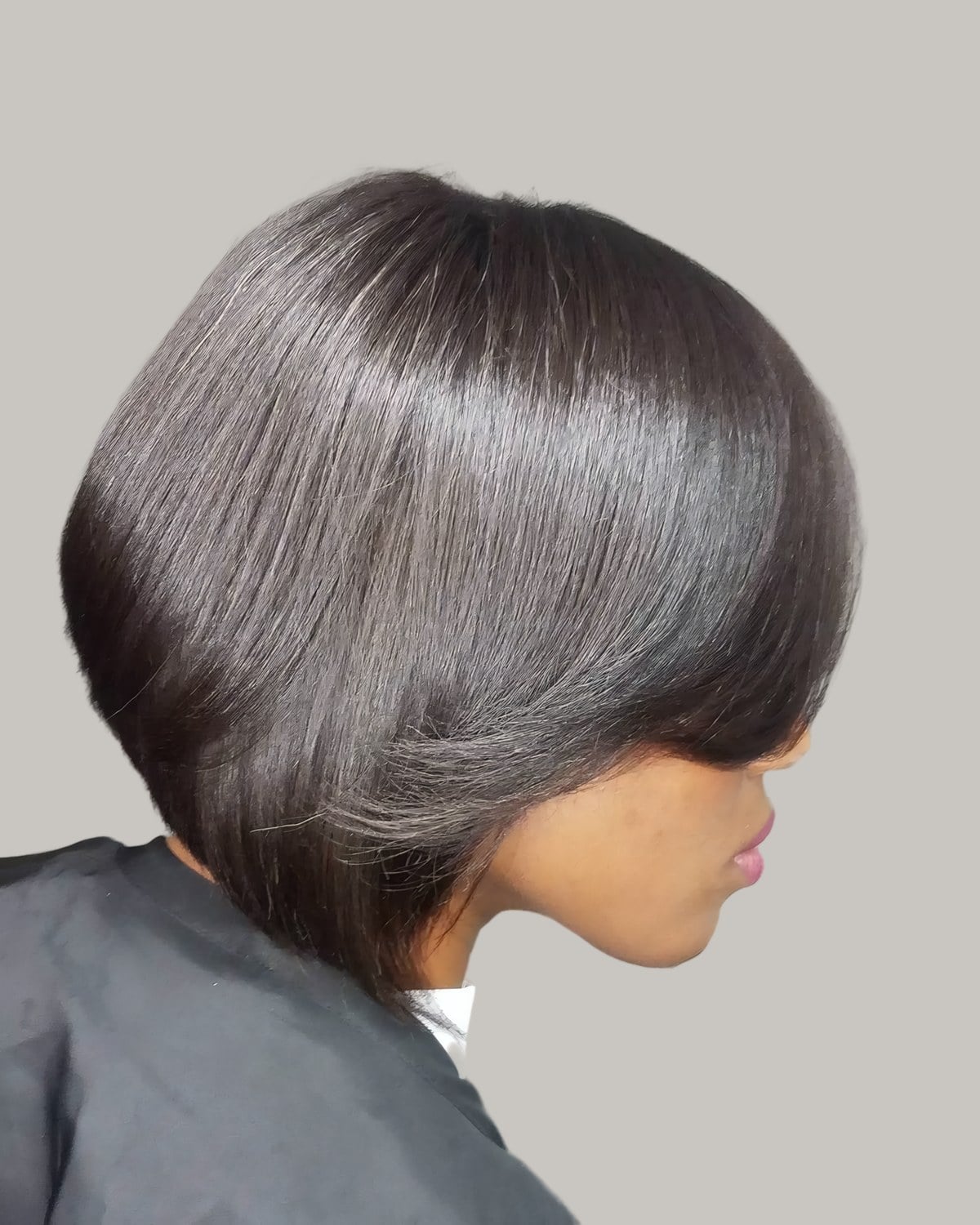 Woman with a glossy black stacked bob in a salon cape, seen in profile