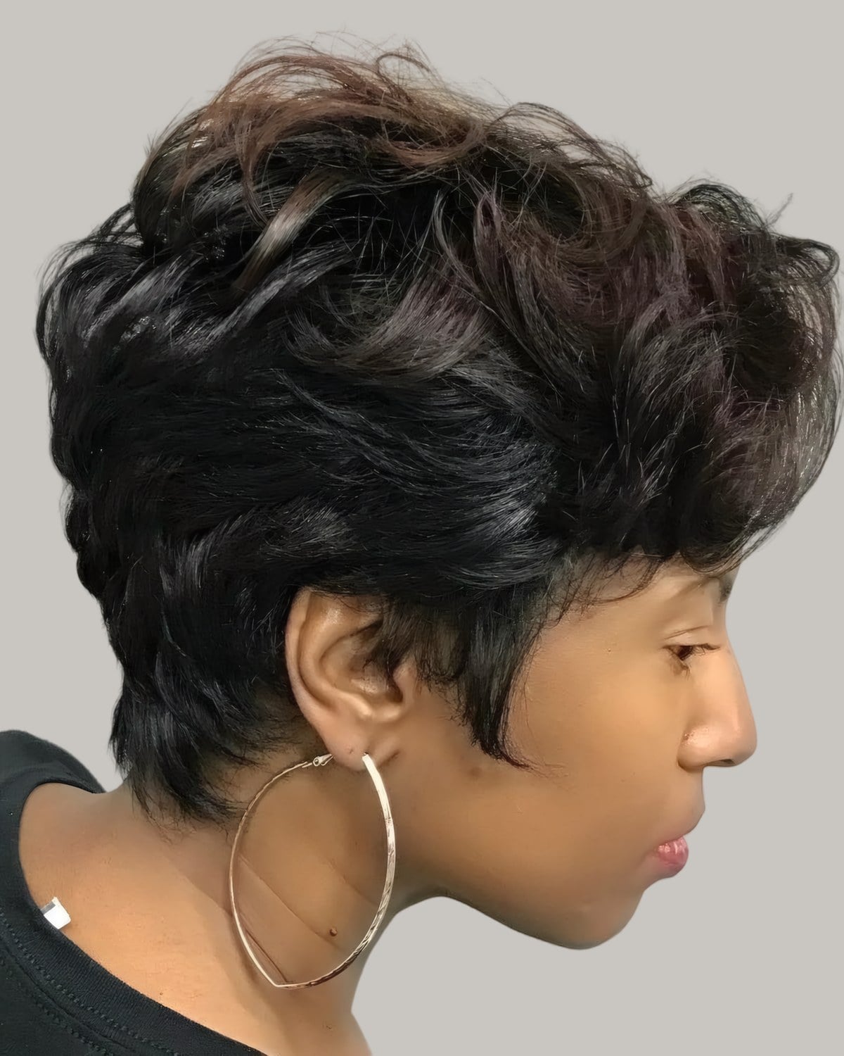 Woman with a dark brown layered pixie and hoop earrings, seen from the side