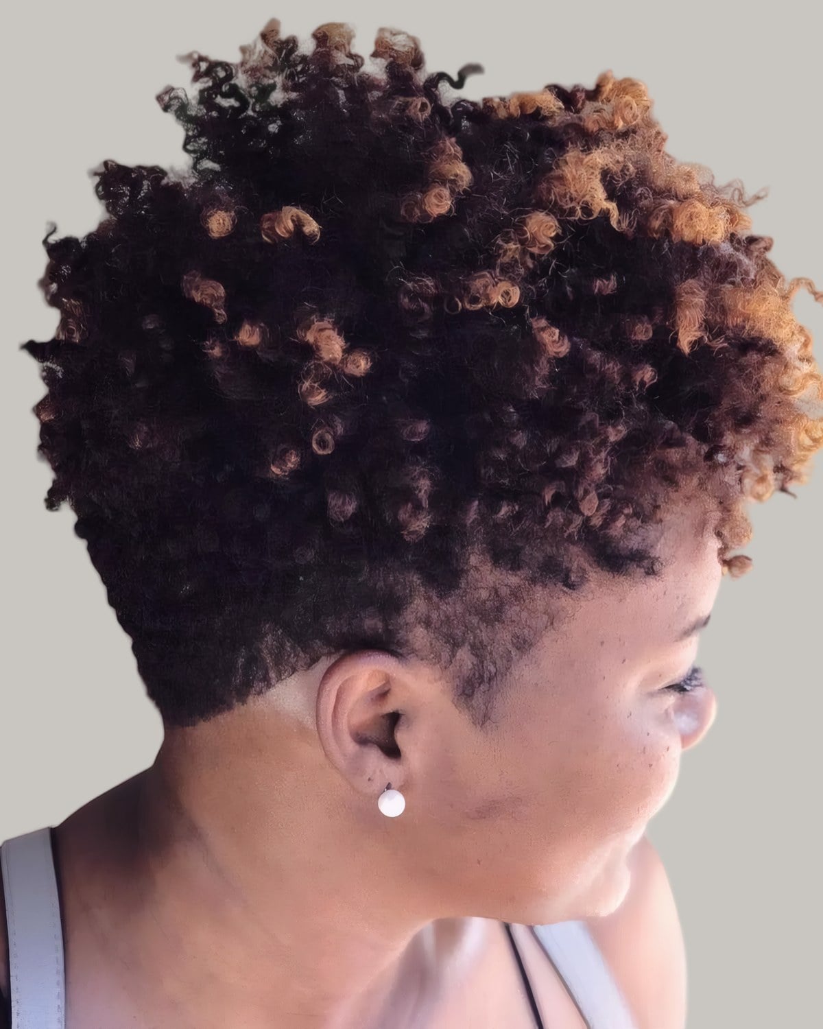 Woman with a dark cropped cut of defined coils, tapered at the neck