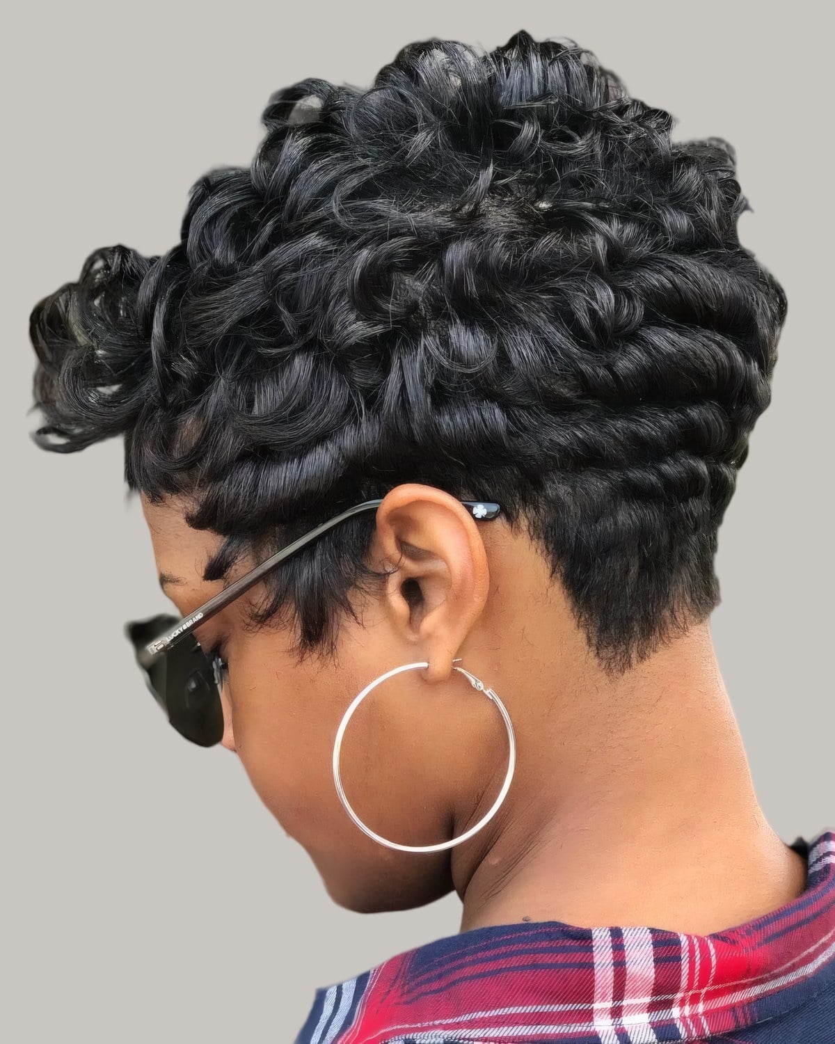 Woman with a black curly pixie and hoop earrings, seen from behind
