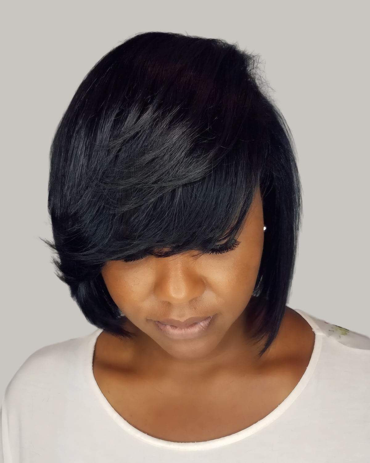Woman with a black ear-length cut and a long bang, looking down