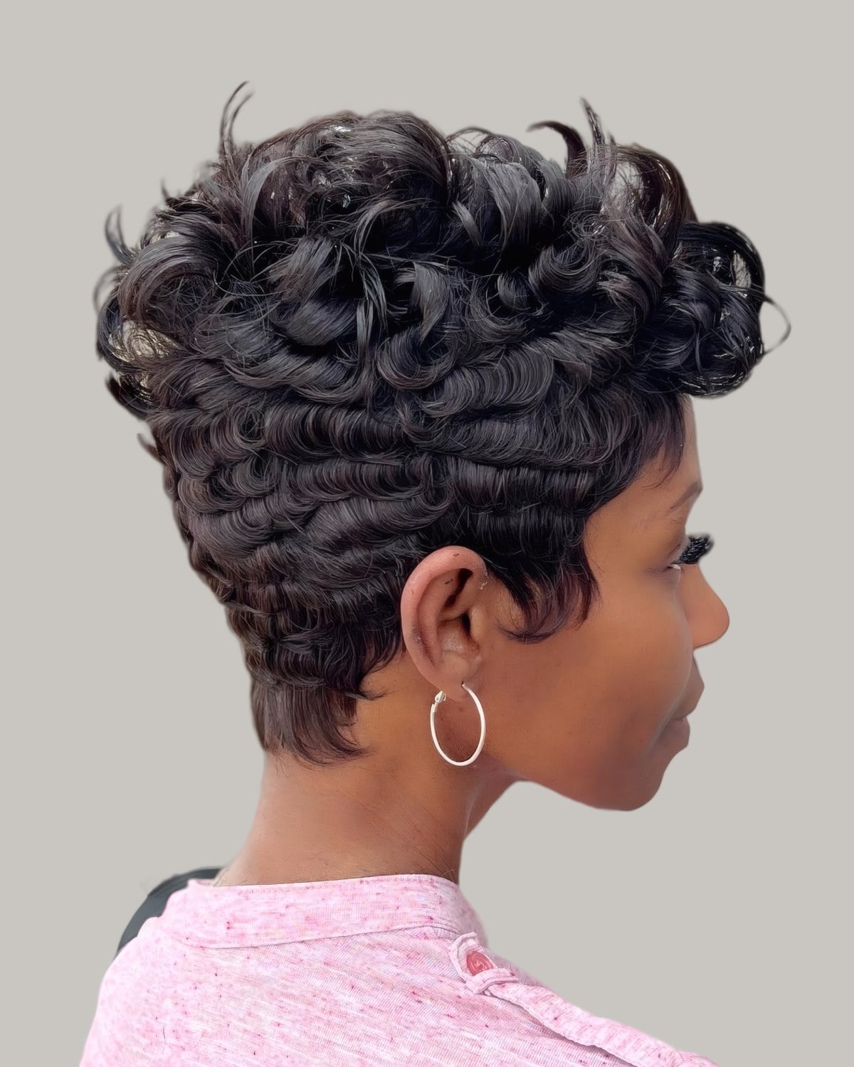 Woman with a short black cut in loose waves and small earrings, looking down