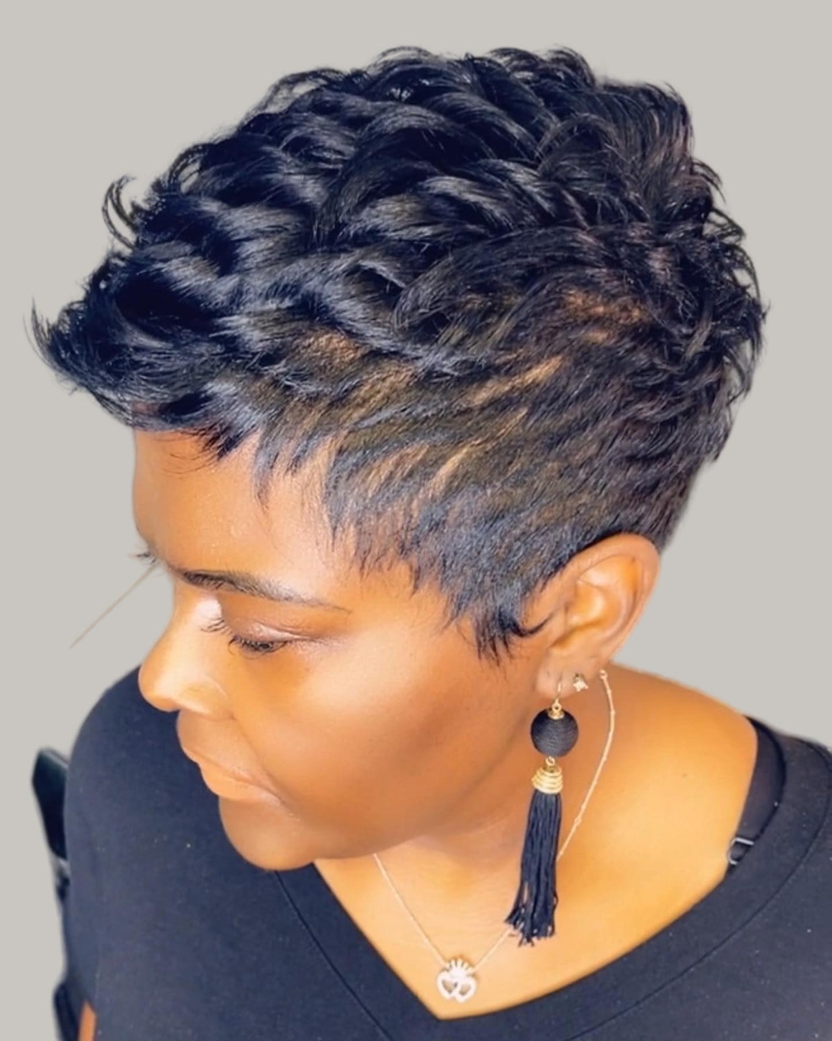 Woman with a blue-black spiky curled pixie, looking down