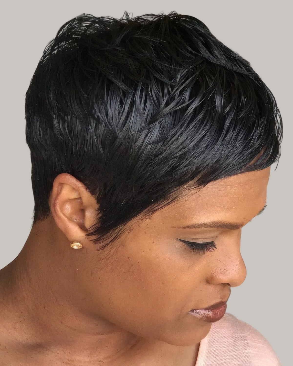 Woman with a sleek black razor-cut pixie, looking down to the side