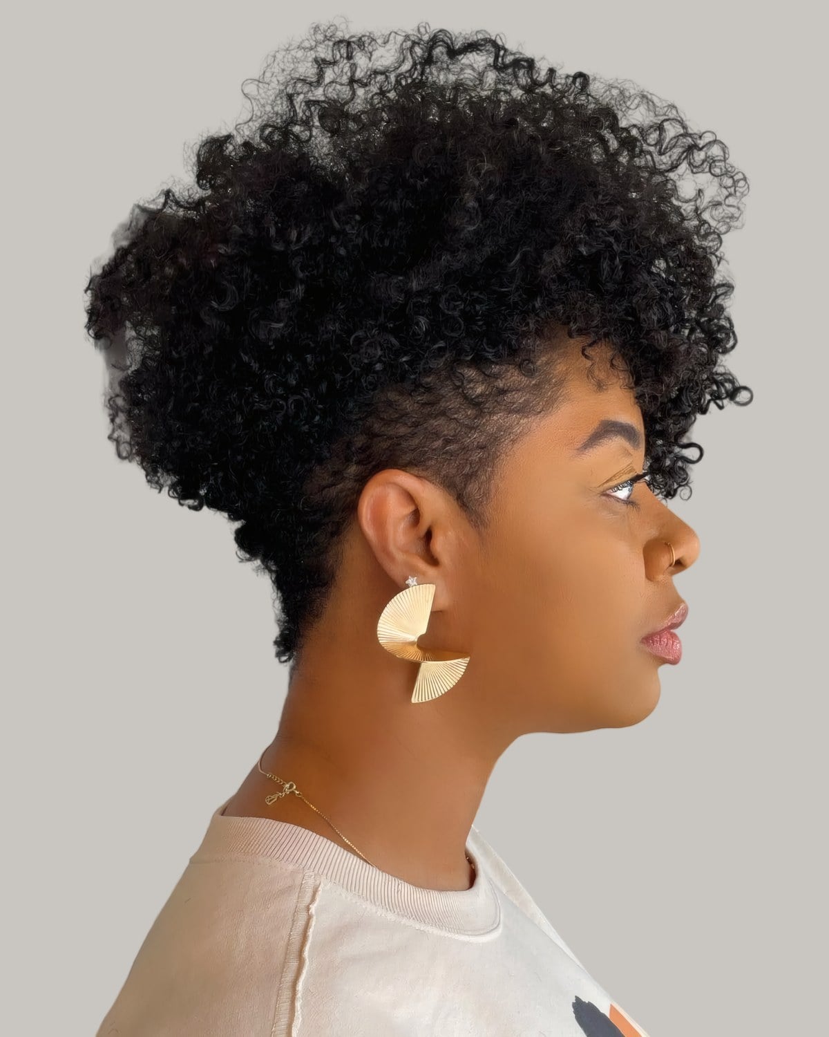 Woman with a black curly mohawk and a tapered side, statement earring