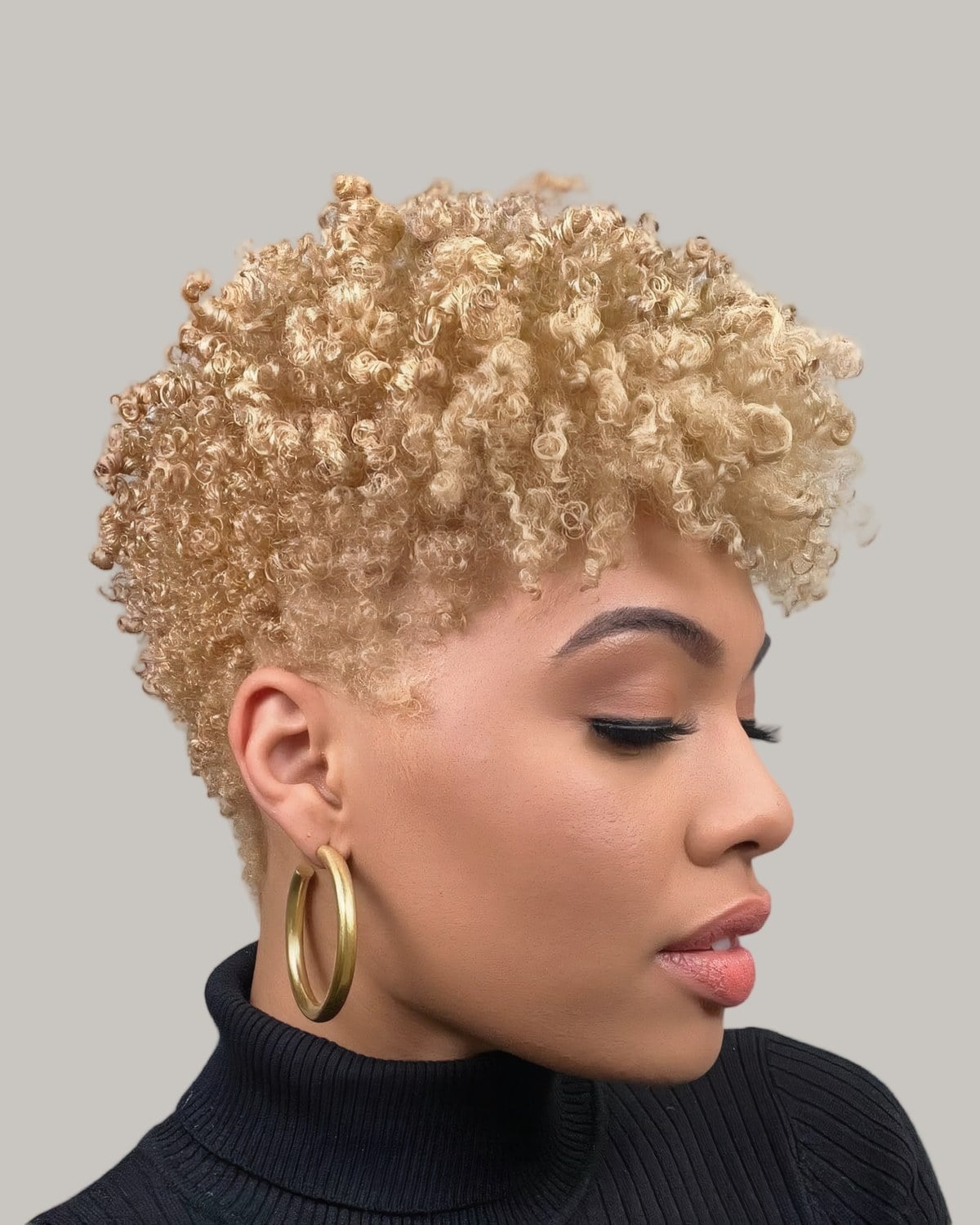 Woman with honey blonde curls on top and hoop earrings, in a black turtleneck