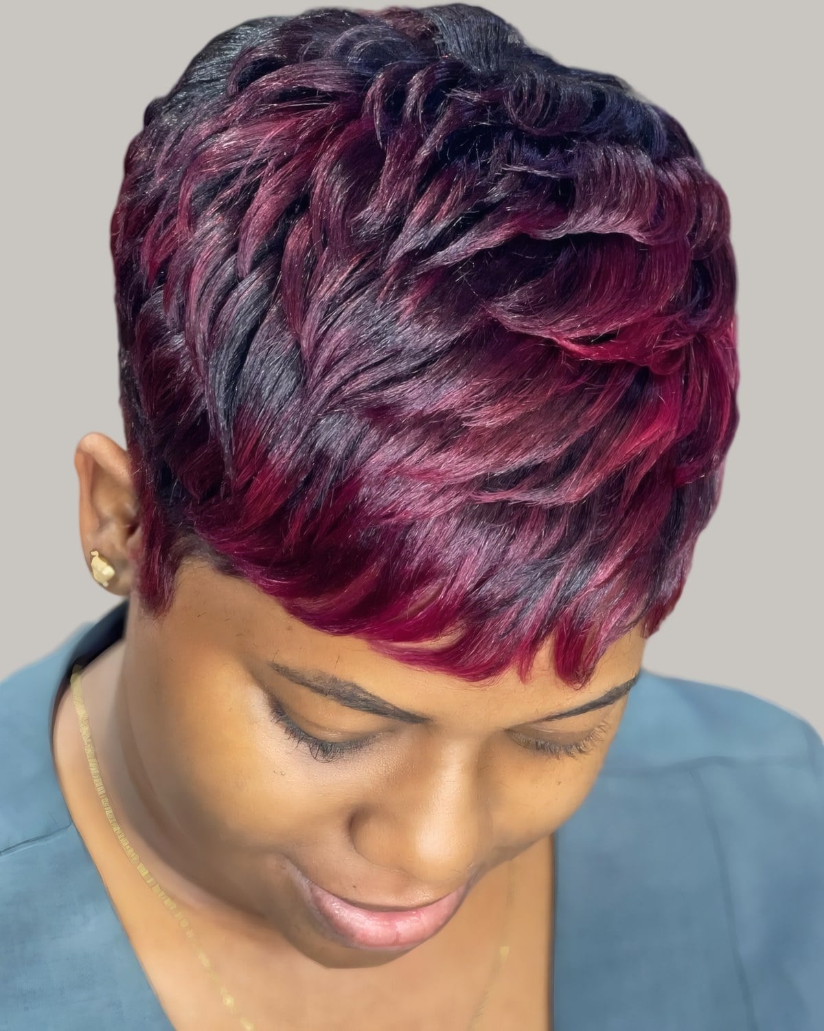 Woman with a burgundy layered short cut with red tips, looking down